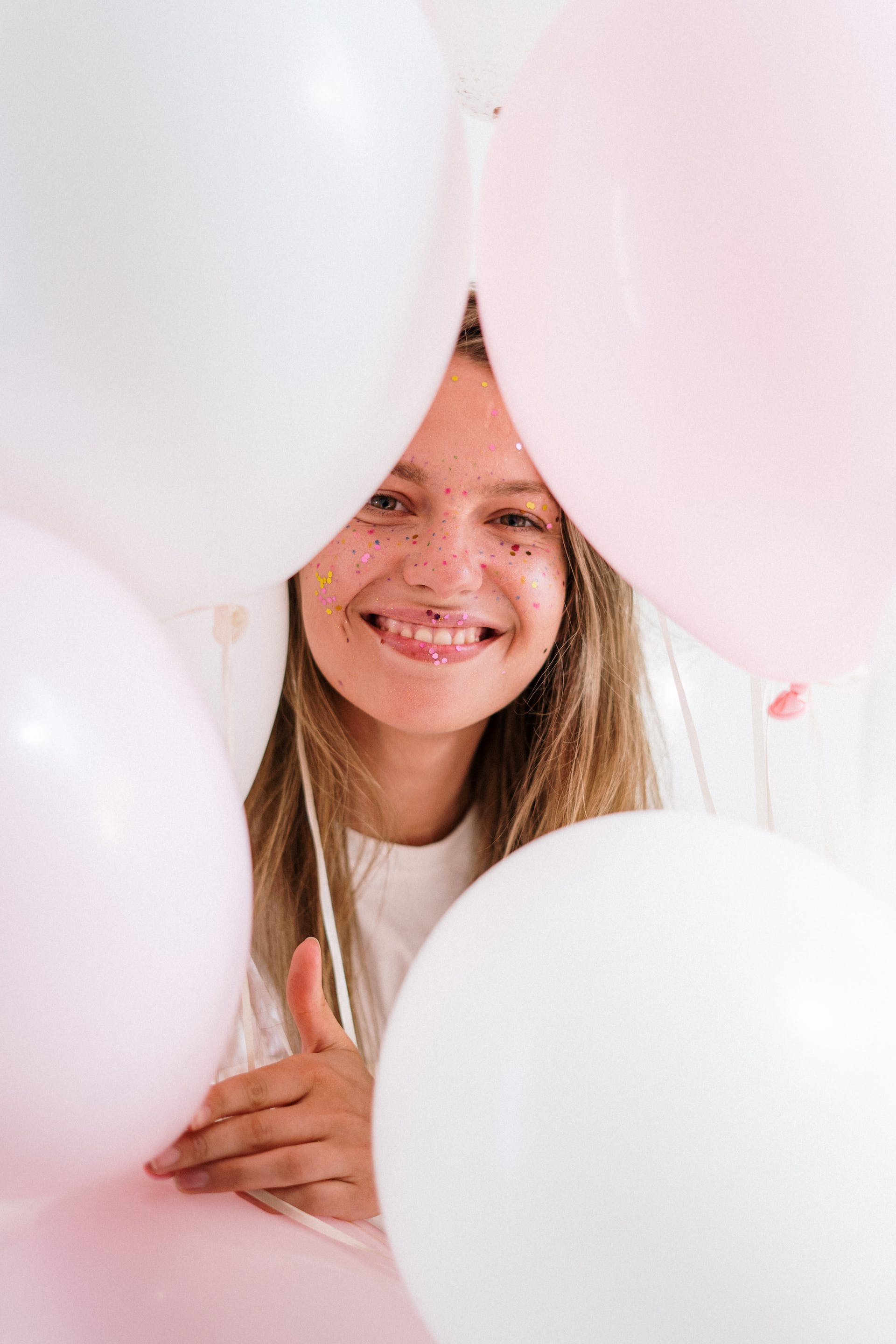 Una niña sonriendo mientras sostiene globos | Foto: Pexels