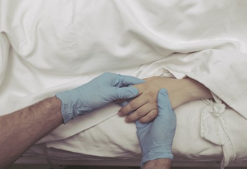 Persona con guantes sostiene la mano de una mujer enferma en una camilla. | Foto: Pixabay