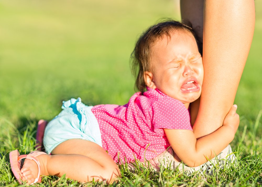 Niña llorando mientras sujeta la pierna de su madre. | Foto: Shutterstock