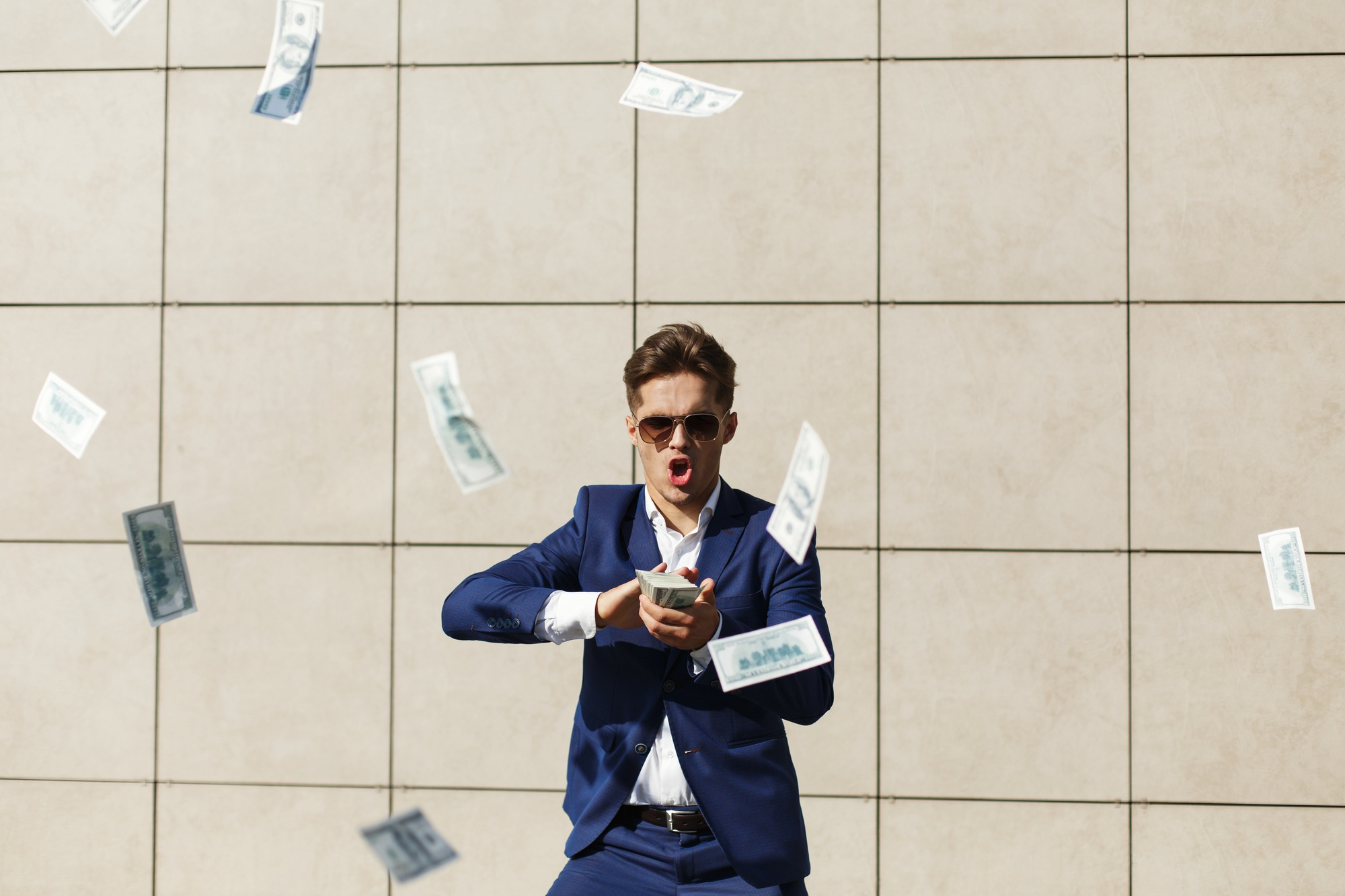 Hombre con gafas de sol y traje mientras tira dinero | Foto: Freepik