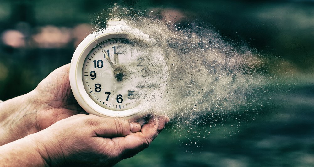 Manos sosteniendo un reloj que se disuelve en pequeñas partículas. | Foto: Shutterstock