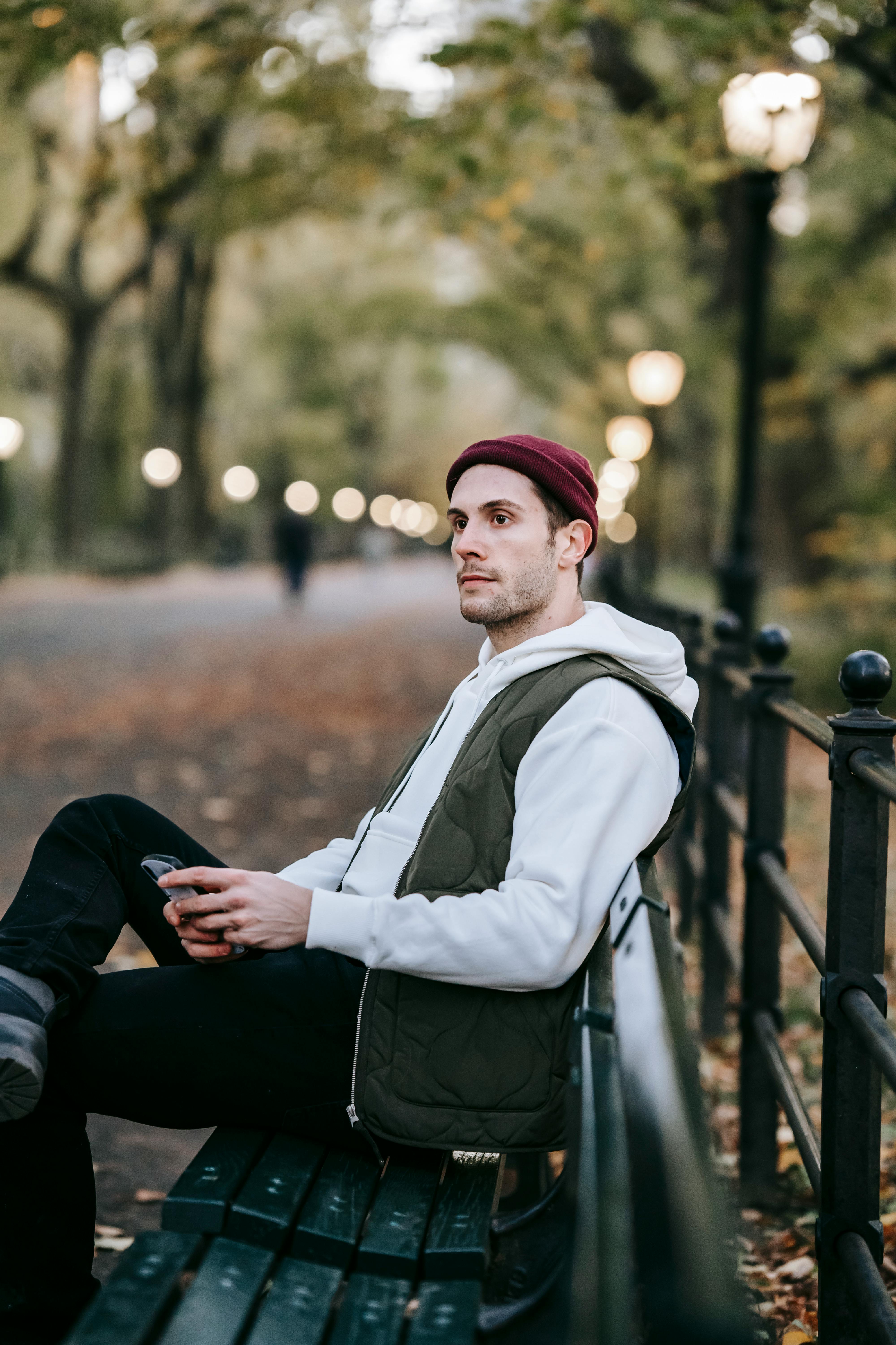 Un hombre sentado en un banco contemplando algo que vio en su teléfono | Foto: Pexels
