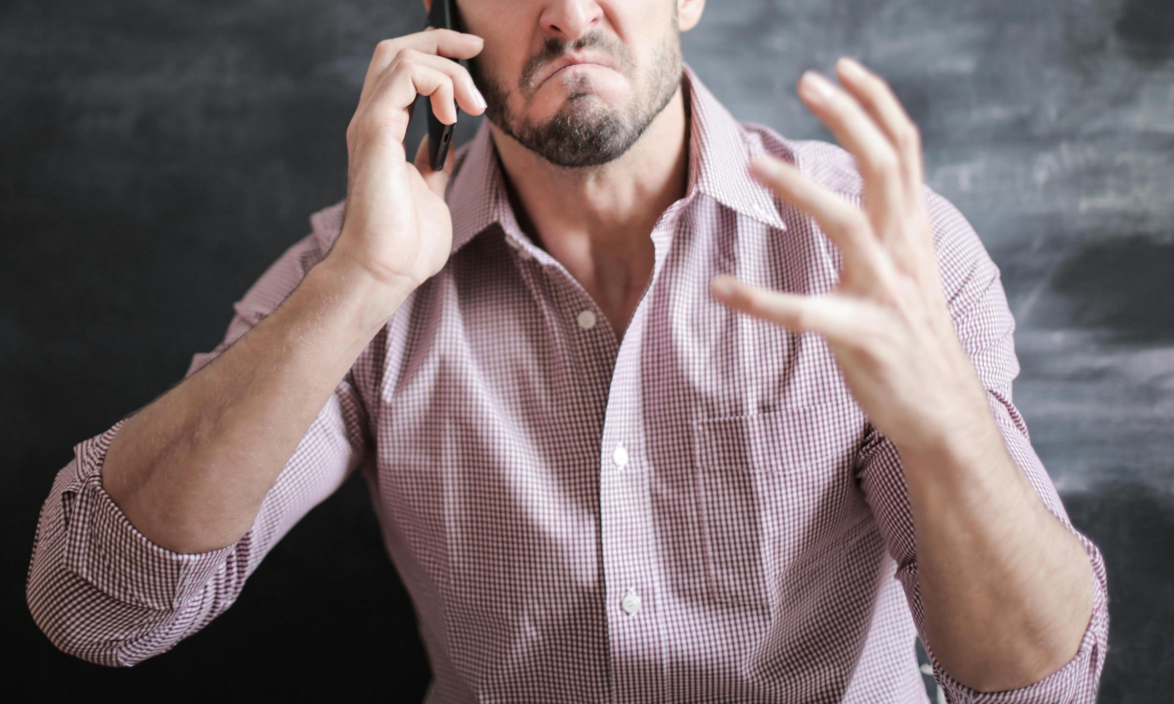 Un hombre reacciona airadamente mientras habla por el móvil | Fuente: Pexels