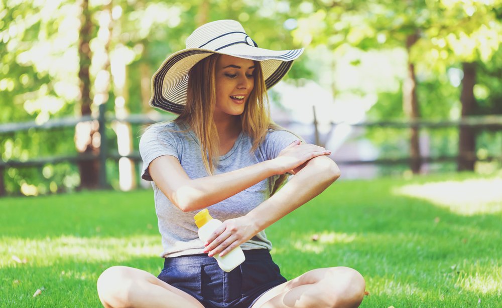Mujer joven con una botella de bloqueador solar en un día de verano. | Fuente: Shutterstock