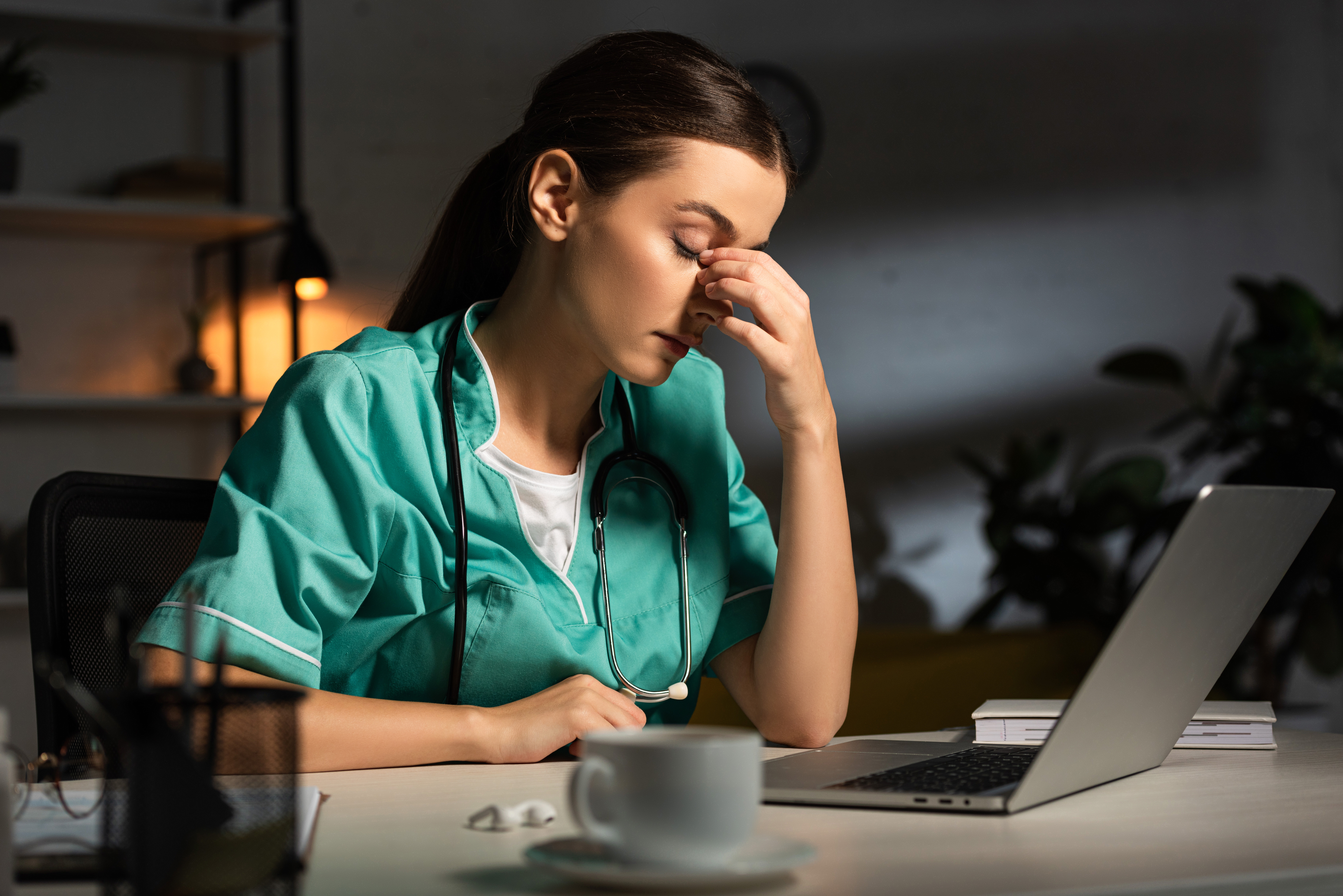 Enfermera cansada con uniforme sentada a la mesa durante el turno de noche | Fuente: Shutterstock.com