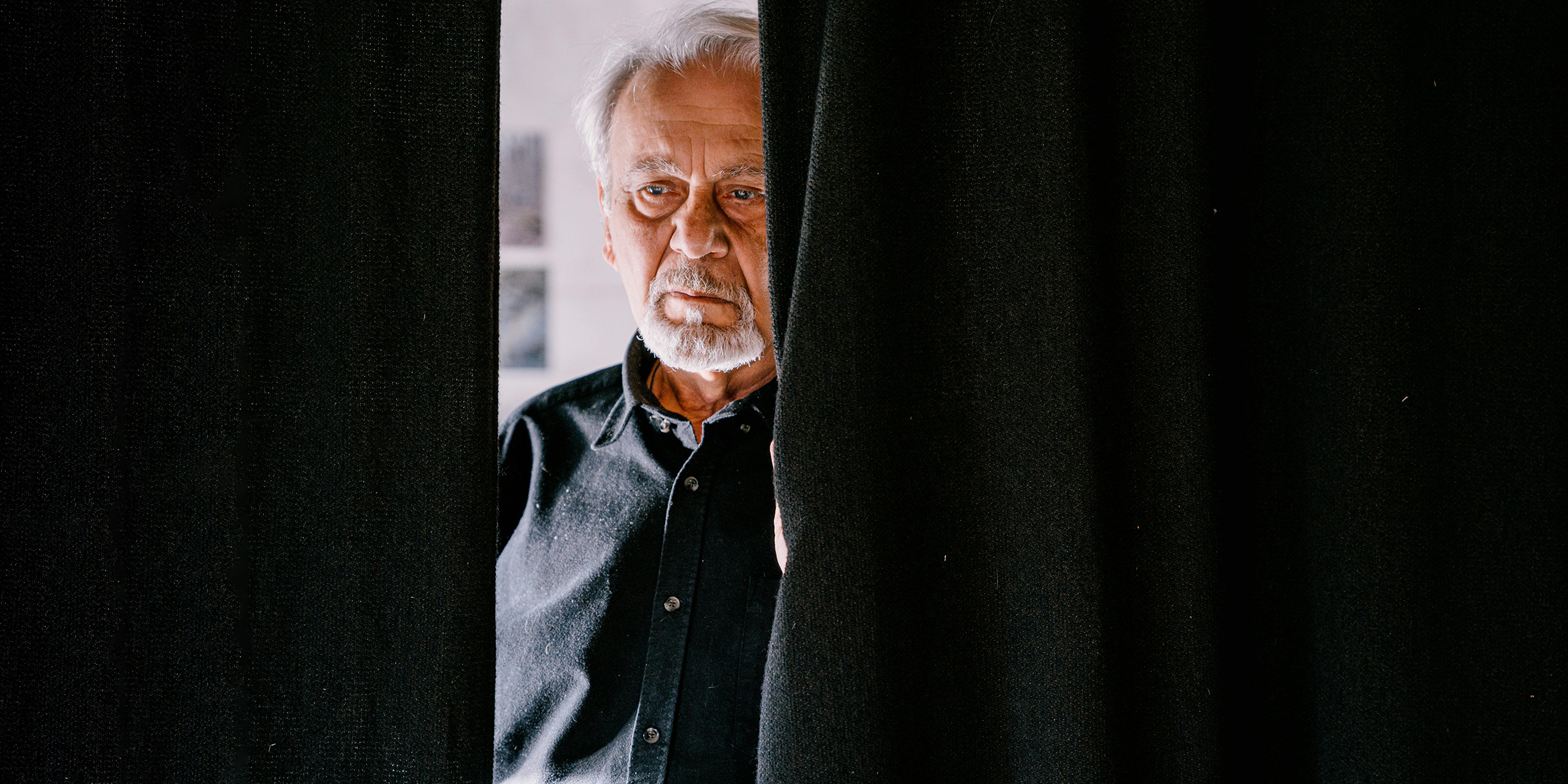 Hombre triste de pie detrás de la cortina | Fuente: Pexels