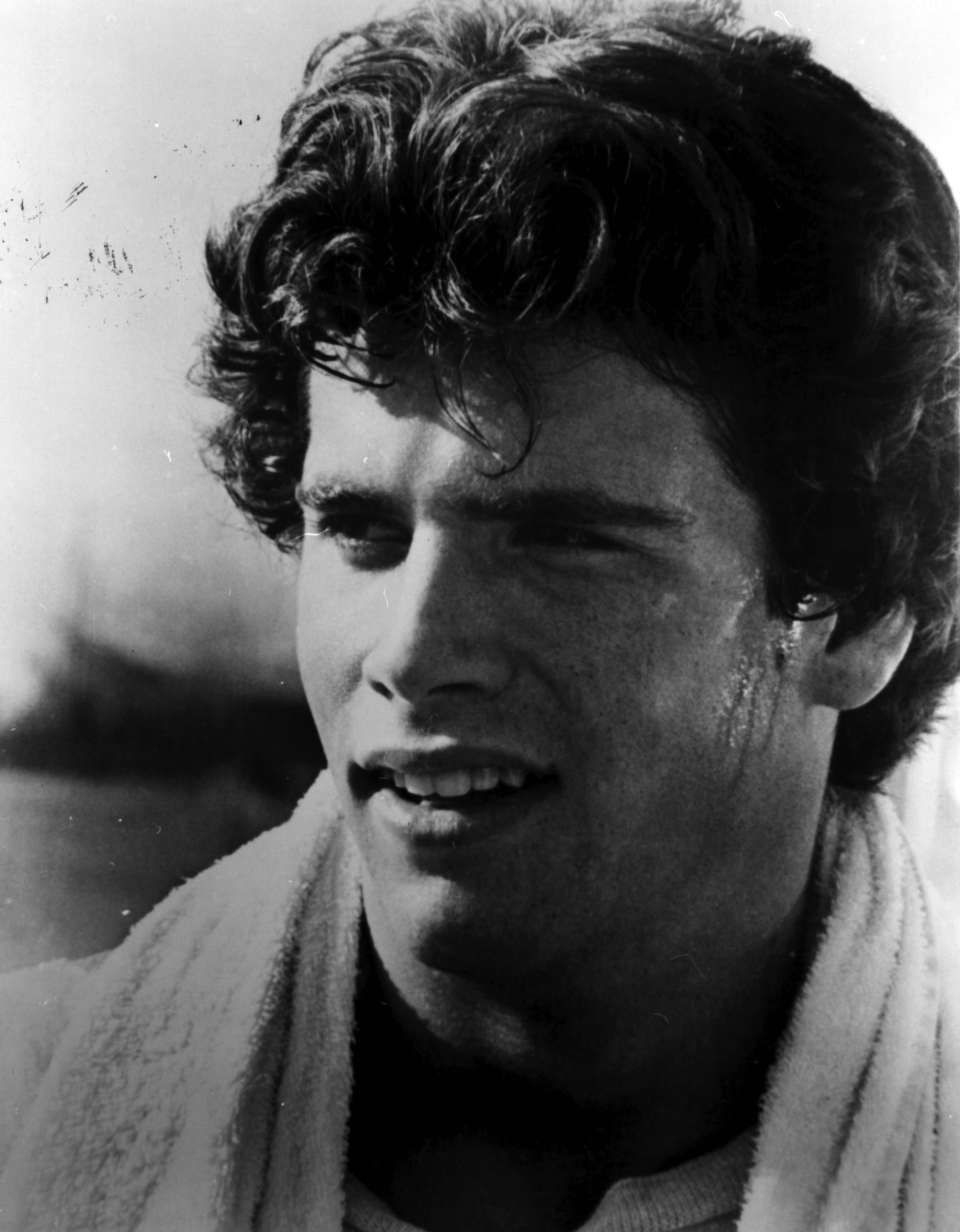El futuro rompecorazones luce su clásico atractivo en un retrato en blanco y negro de aire melancólico de los años 70. Con el sudor brillando en la sien y la mandíbula, mira pensativo hacia un lado, con su espesa melena oscura y ondulada y una toalla blanca de rizo colgada al cuello. | Fuente: Getty Images