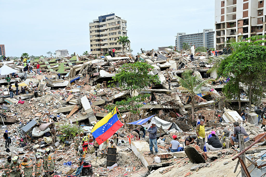 Miembros de una unidad de rescate del Ejército mexicano y voluntarios trabajan entre los escombros de edificios derrumbados mientras una bandera venezolana ondea en Caraballeda, estado de La Guaira, Venezuela, el 3 de julio de 2026. | Fuente: Getty Images