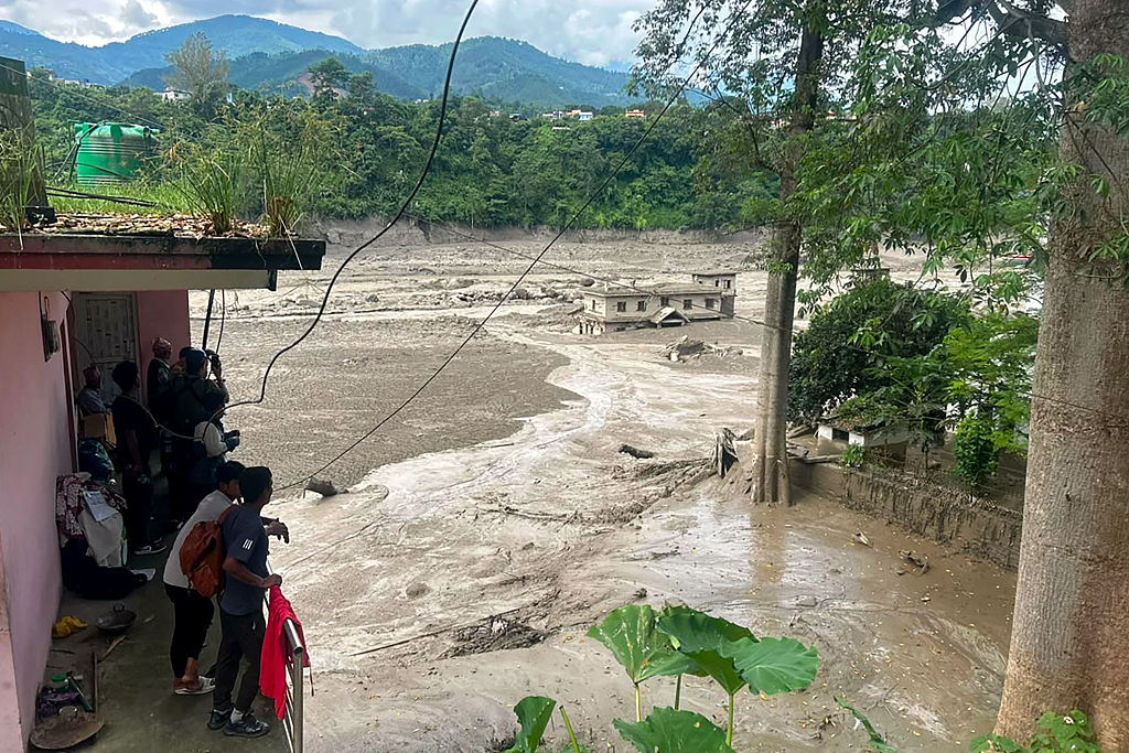 Residentes observan cómo un torrente de agua turbia recorre un río tras las inundaciones repentinas en Trishuli Bazar, en el distrito de Nuwakot, Nepal, el 26 de agosto de 2026. | Fuente: Getty Images