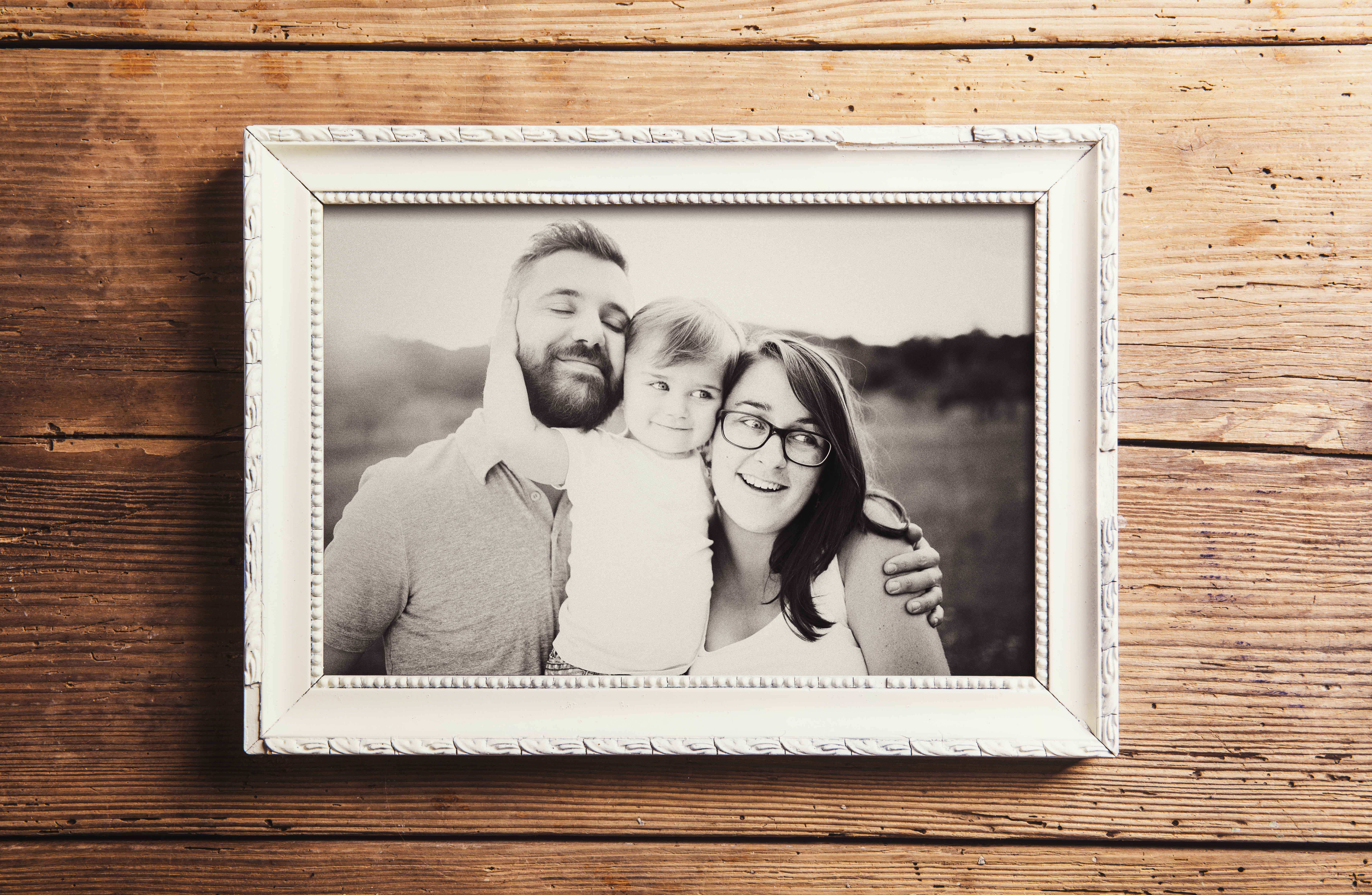 Fotografía en escala de grises de una familia de tres miembros en un marco de madera | Fuente: Shutterstock