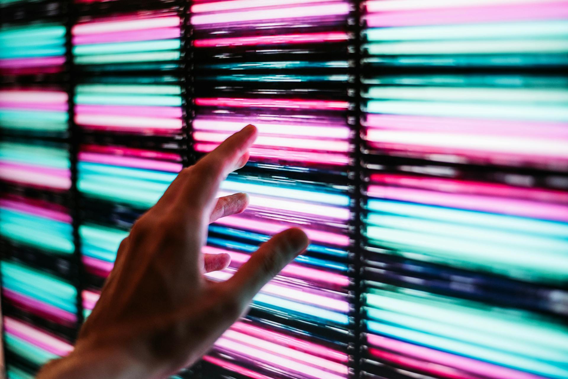 Una persona a punto de tocar un panel LED azul y rosa | Fuente: Pexels