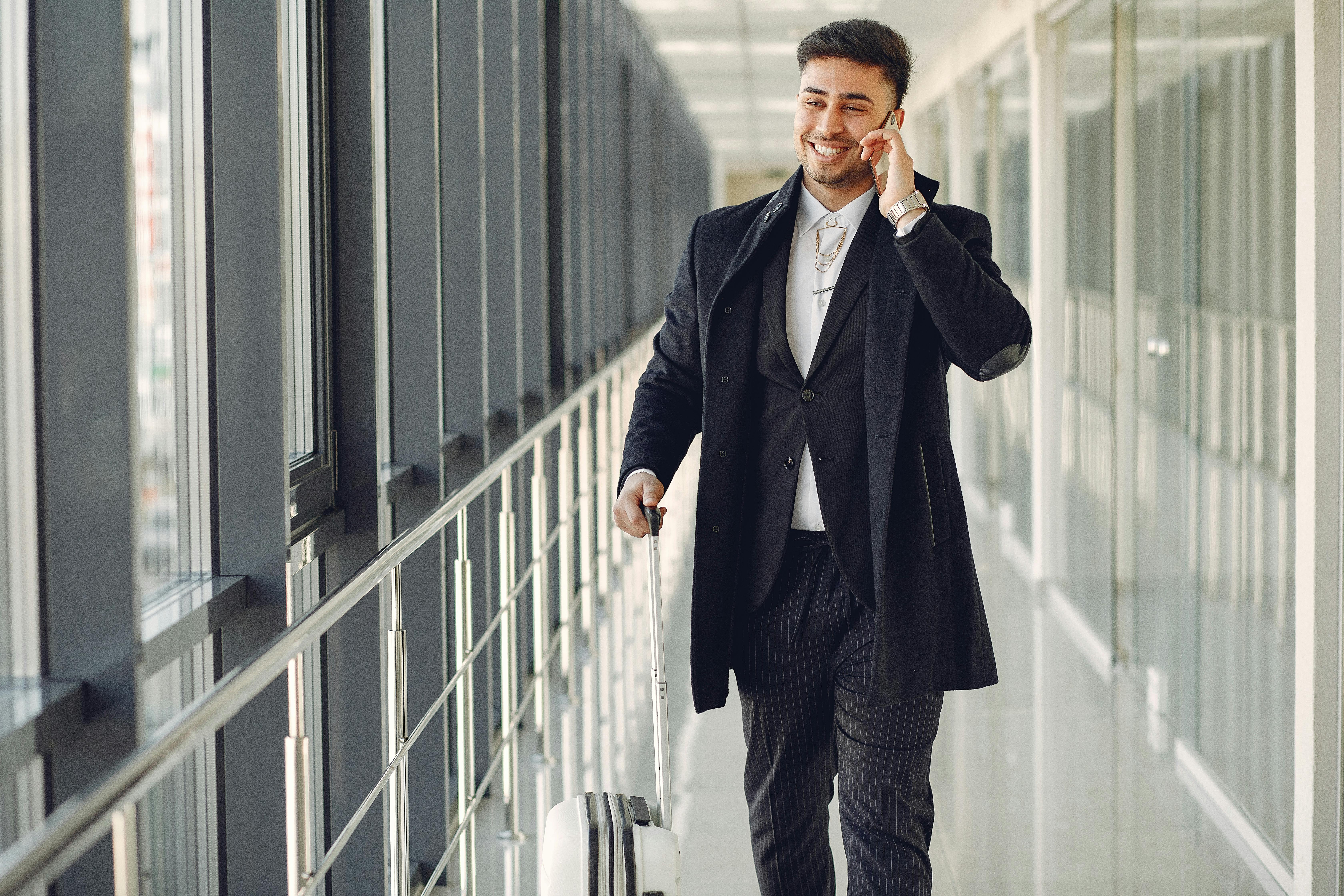 Un hombre feliz hablando por teléfono mientras camina con su equipaje | Fuente: Pexels