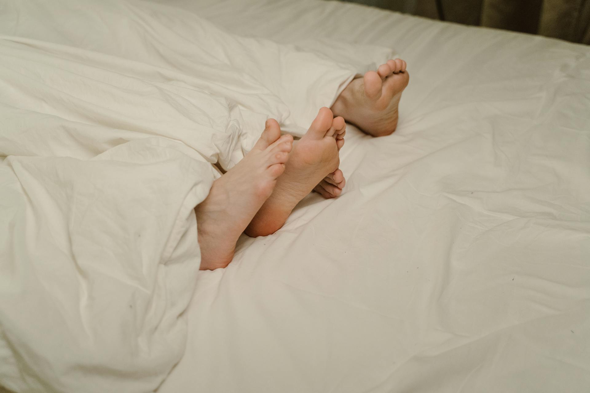 Pies de personas que sobresalen de las sábanas | Fuente: Pexels
