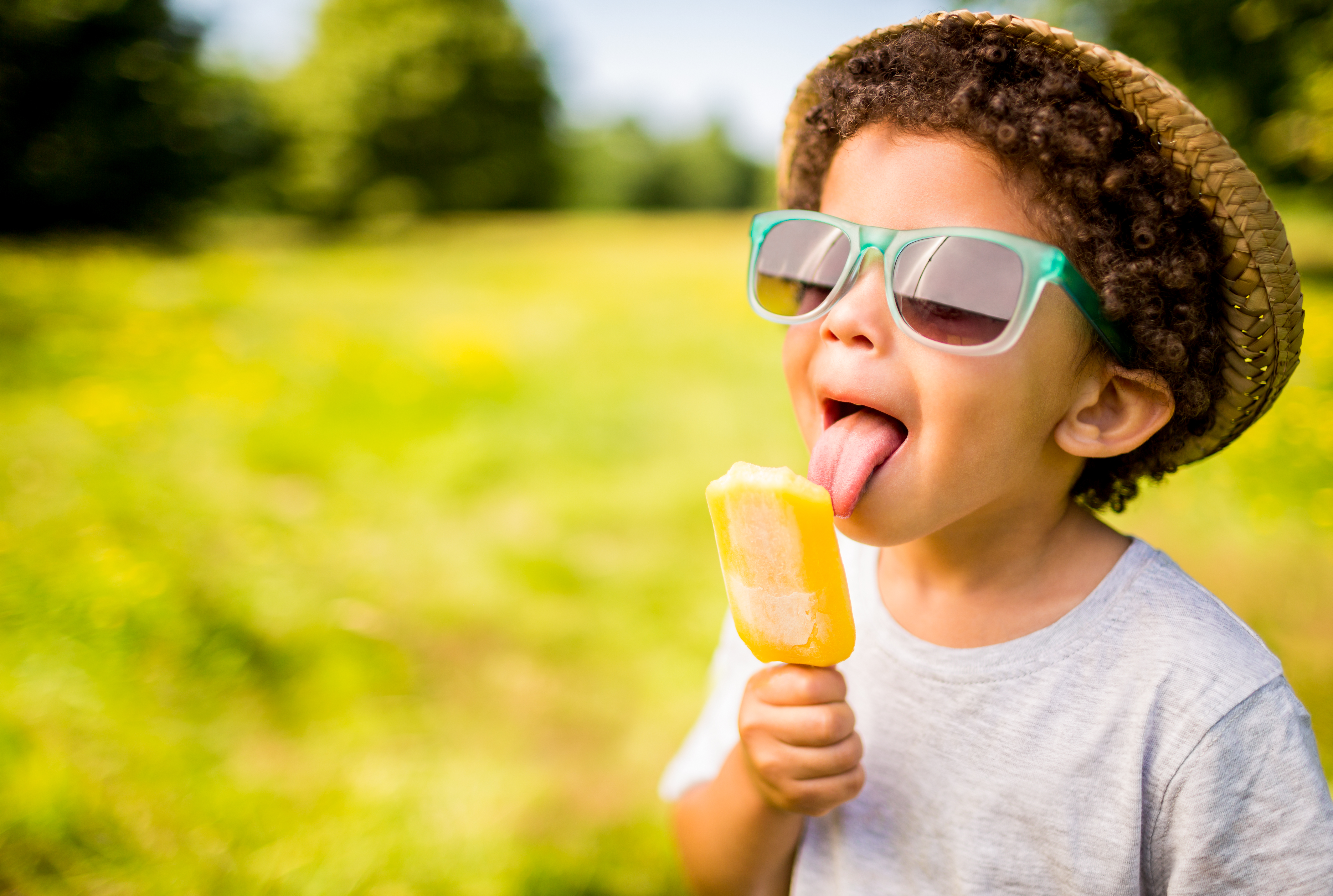 Niño con gafas de sol y sombrero comiendo un polo al aire libre | Fuente: Getty Images