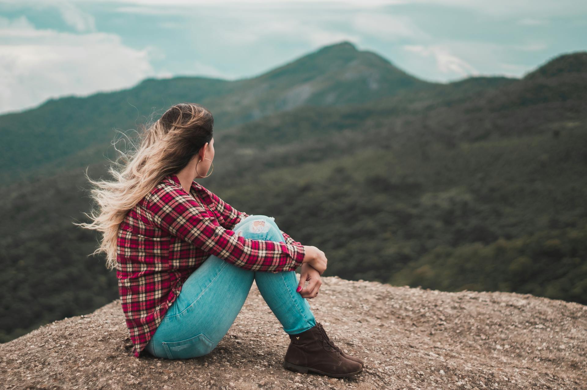 Vista lateral de una mujer sentada en el suelo con vistas a una colina | Fuente: Pexels