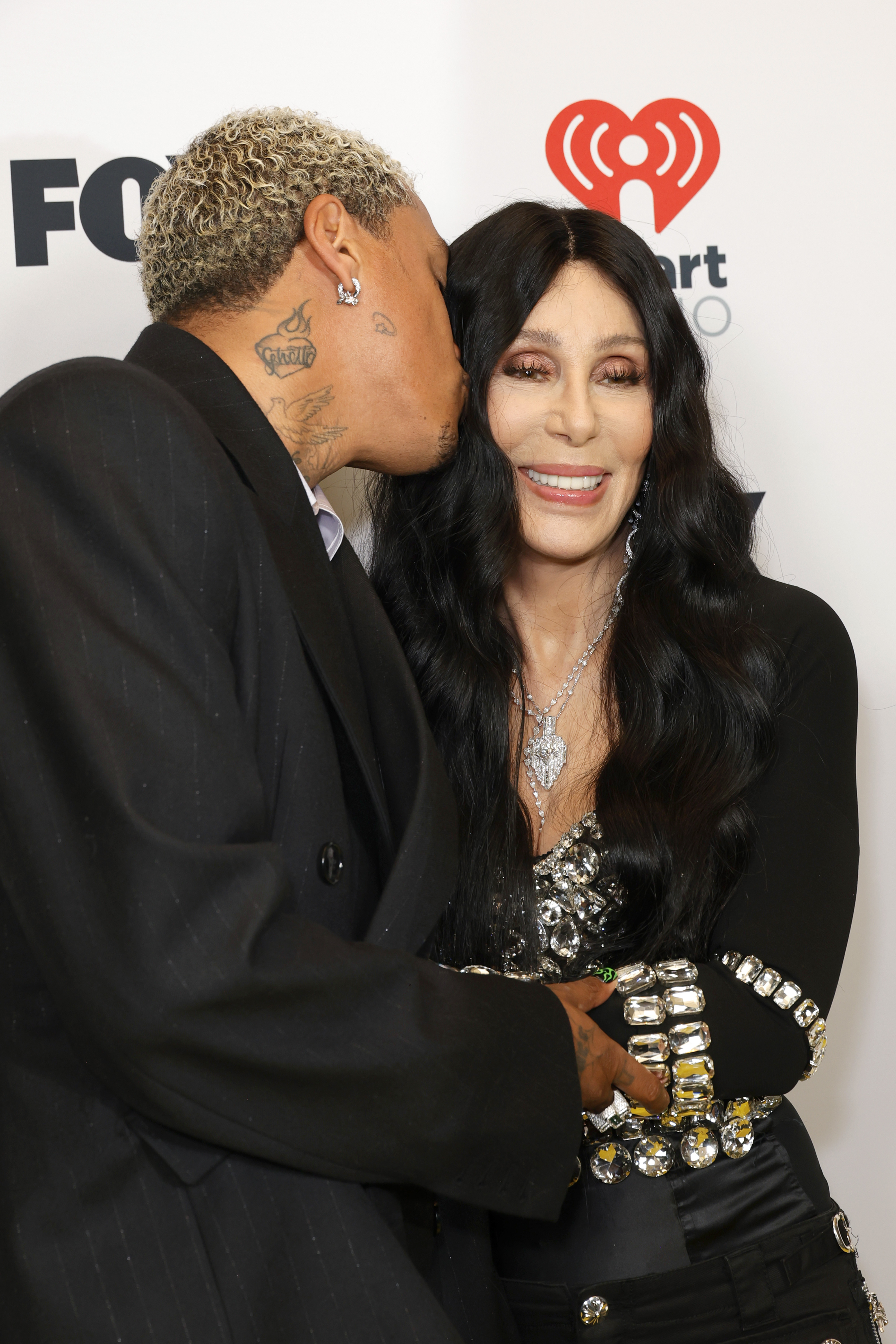 Alexander "AE" Edwards besa a Cher en la mejilla en los 2024 iHeartRadio Music Awards el 1 de abril de 2024 en Hollywood, California. | Fuente: Getty Images