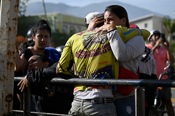 Personas reaccionan junto a un edificio de apartamentos dañado tras el terremoto ocurrido en Catia La Mar, estado La Guaira, a unos 30 kilómetros al noroeste de Caracas, el 25 de junio de 2026, mientras lamentan la muerte de un familiar. Los dos sismos, los más fuertes registrados en Venezuela en más de un siglo, dejaron al menos 164 muertos y destruyeron numerosos edificios cerca de la capital, donde los habitantes continuaban buscando a sus familiares desaparecidos.