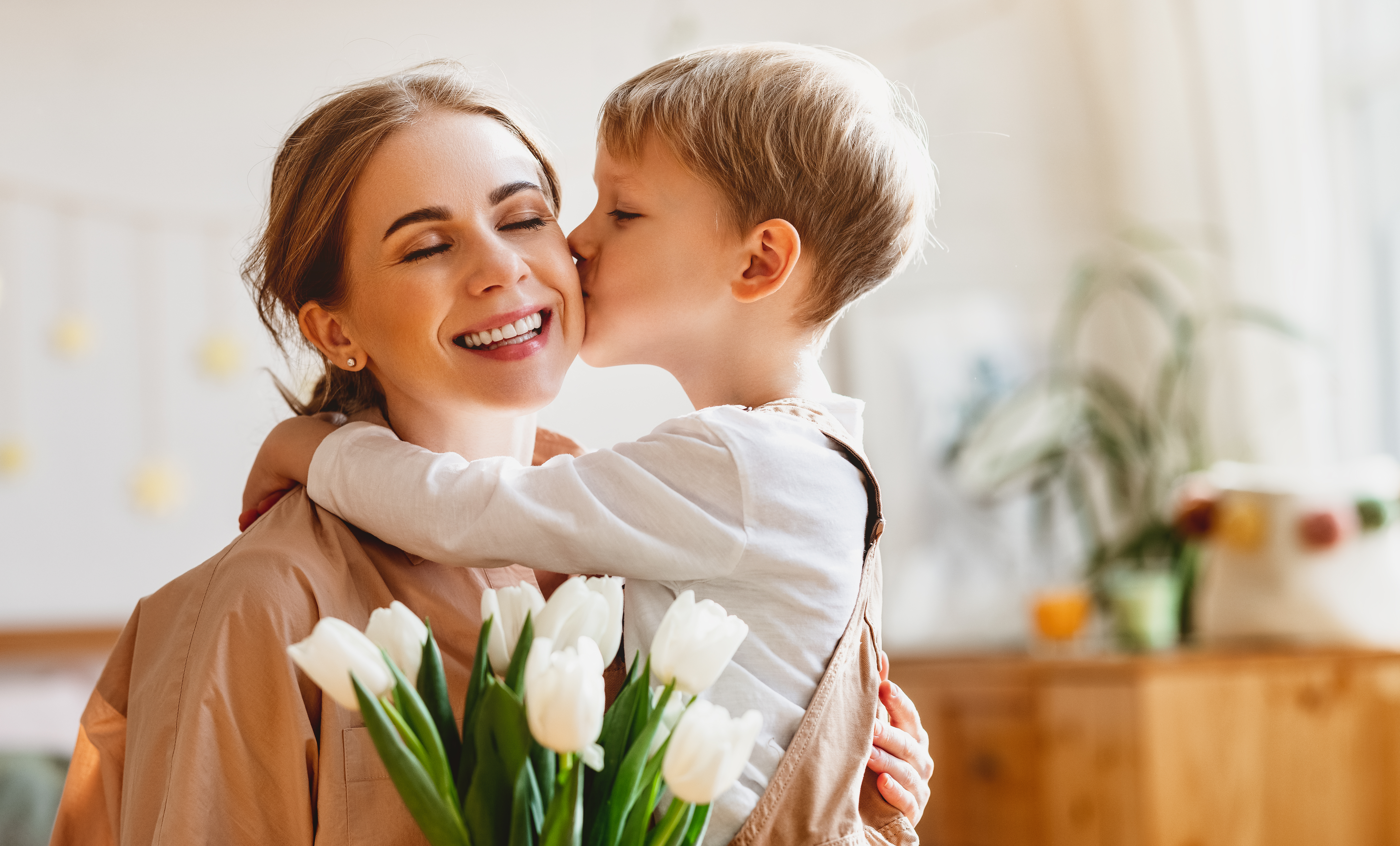 Niño besando a su madre y regalándole flores | Fuente: Shutterstock