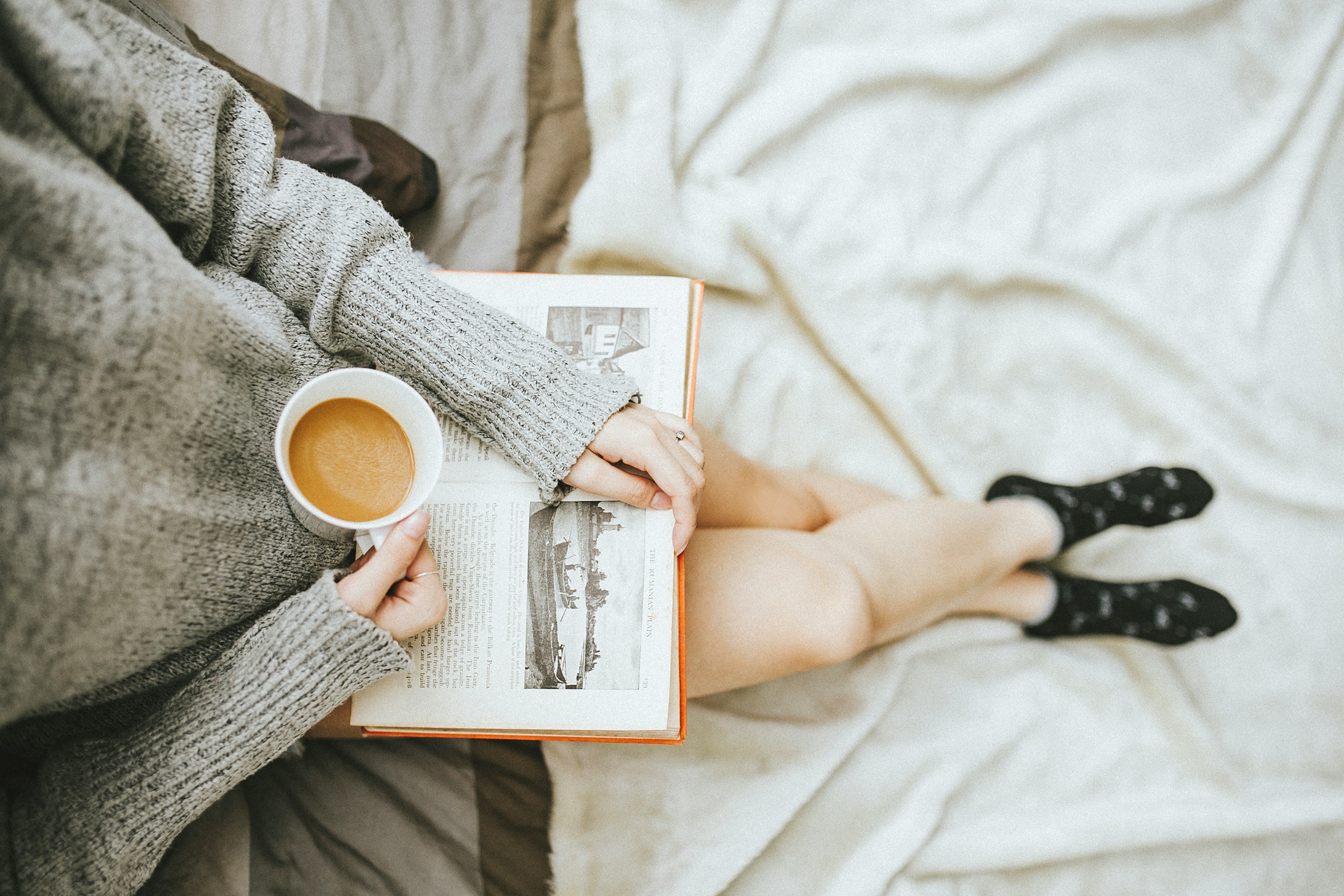Una mujer leyendo un libro mientras disfruta de una taza de café en casa | Foto: Unsplash