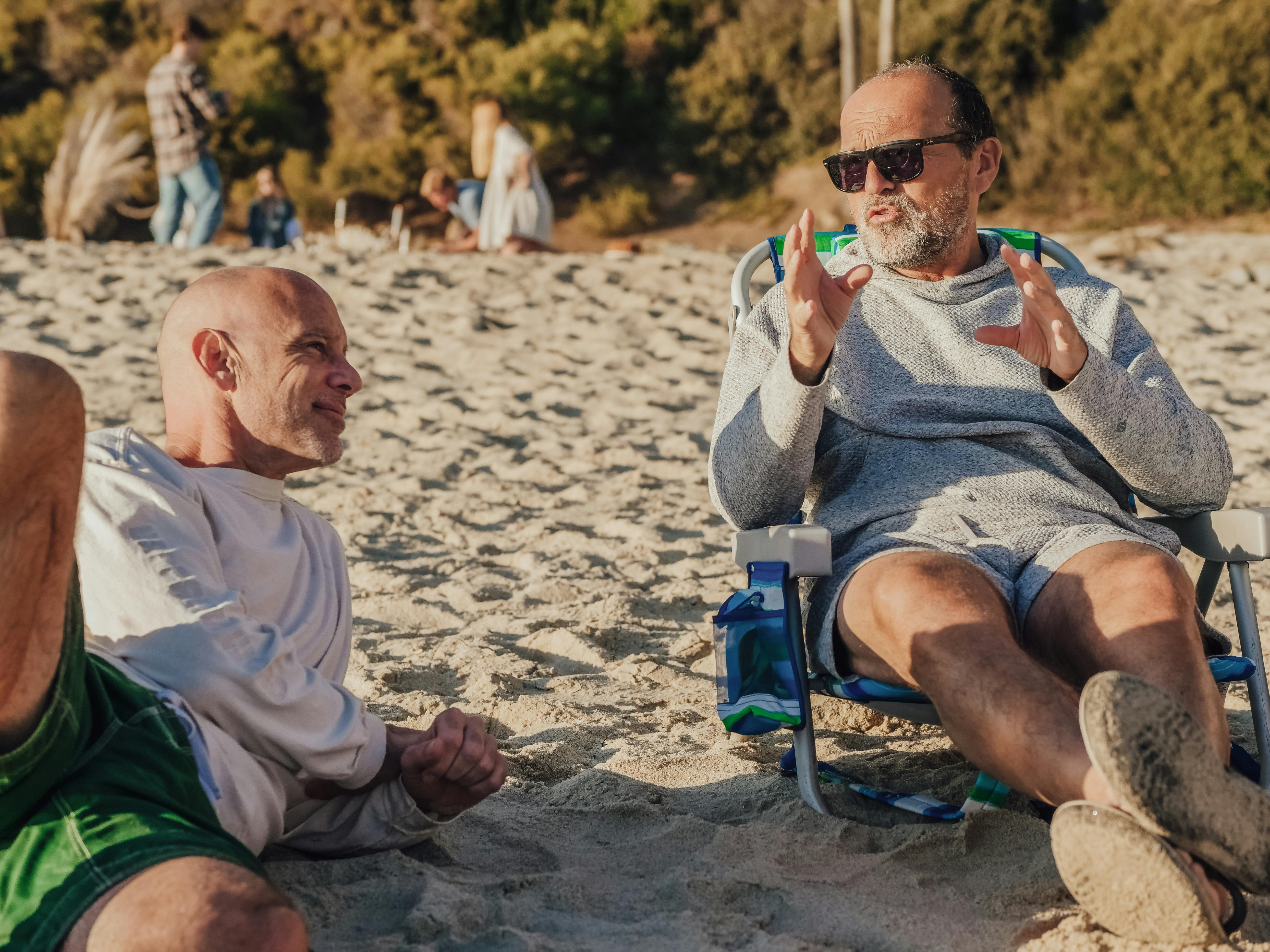 Un hombre de mediana edad presumiendo de algo ante otro hombre en la playa | Foto: Pexels