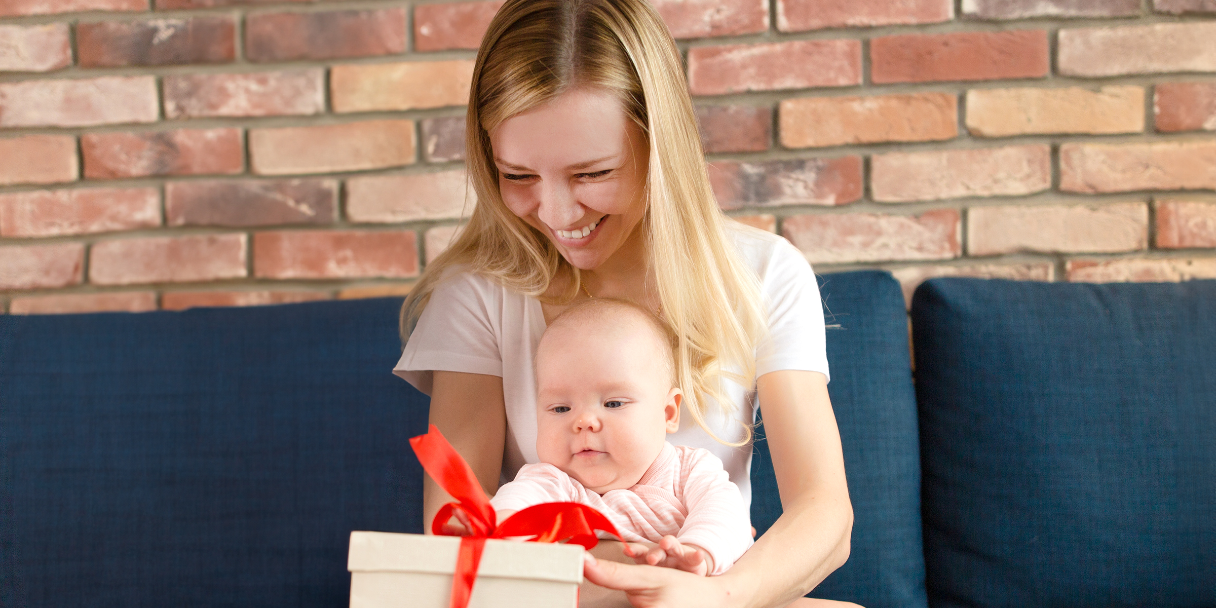 Una mujer sonriente con un bebé en brazos y una caja de regalo | Fuente: Shutterstock