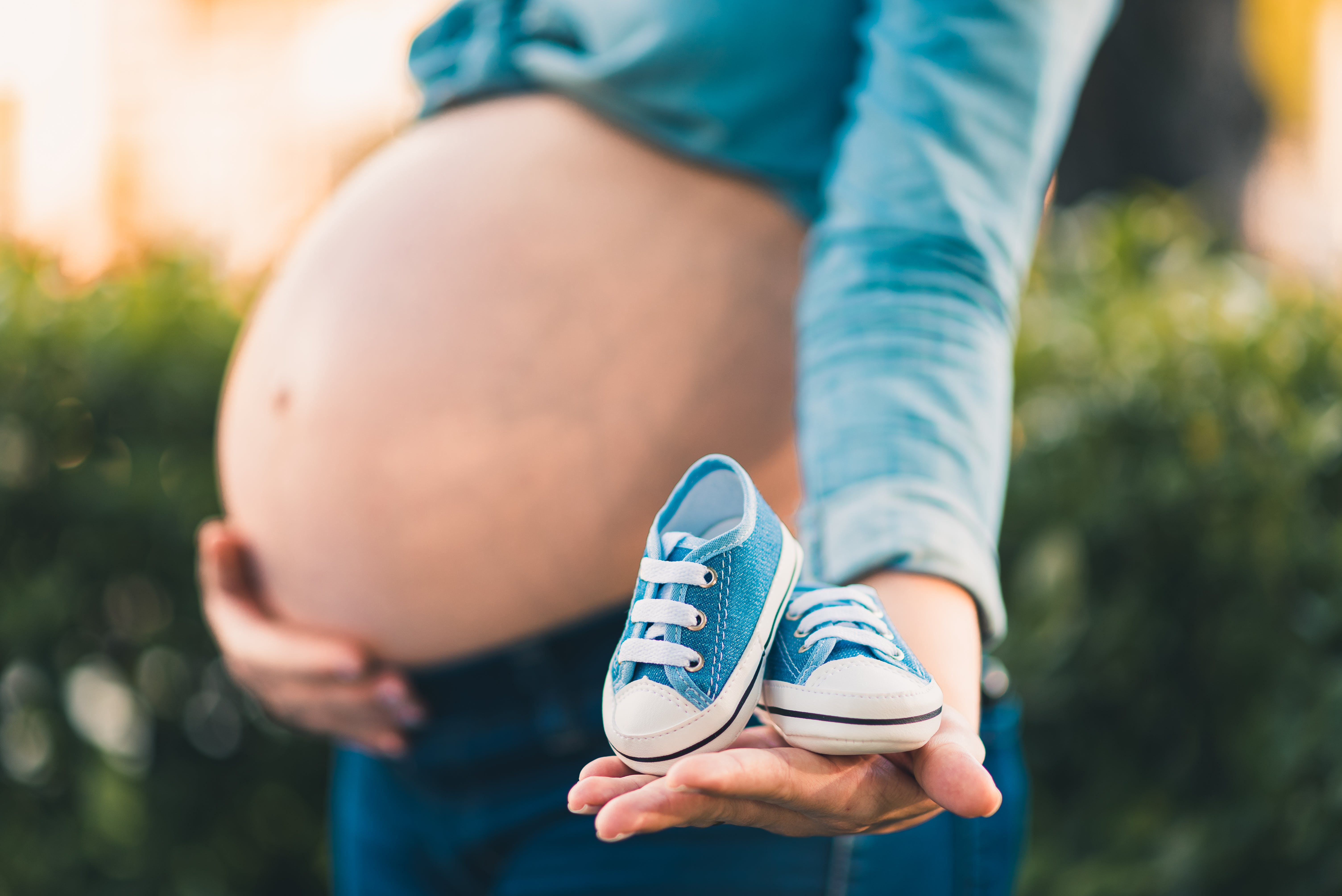 Una mujer embarazada con la barriga en una mano y unas zapatillas azules de bebé en la otra | Foto: Pexels