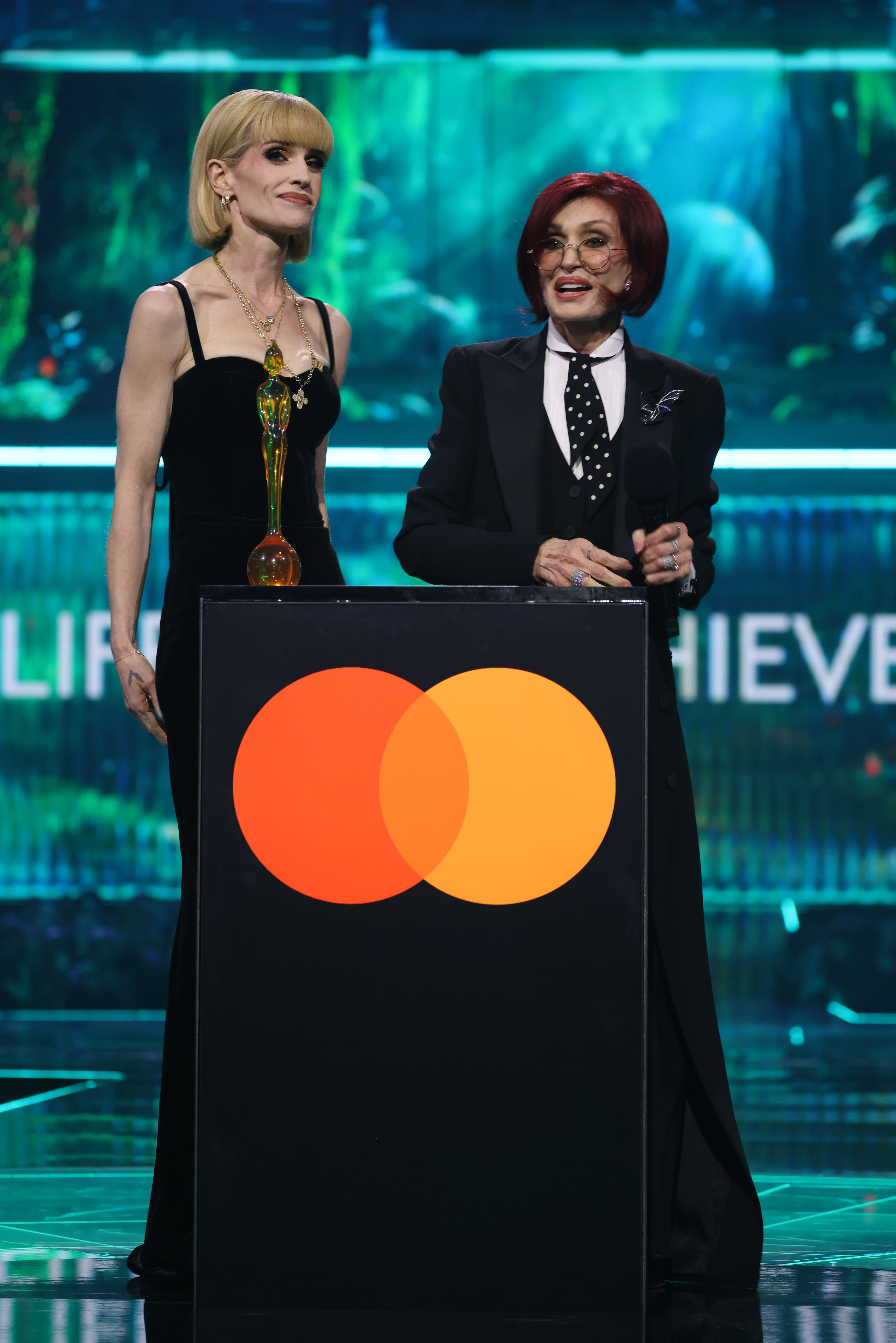 Sharon Osbourne se dirigió al público en los BRIT Awards de 2026 mientras Kelly estaba a su lado, escuchando, en el momento en que rendían homenaje al legado de Ozzy y recogían su Premio a toda una carrera, otorgado a título póstumo. | Fuente: Getty Images.