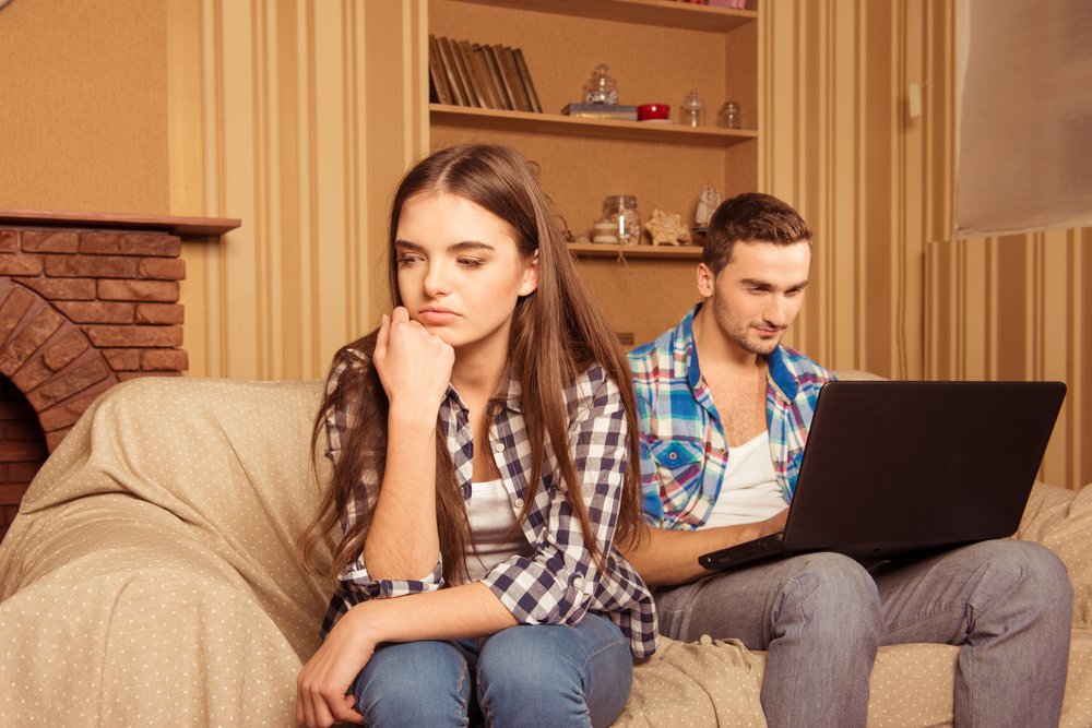 Hombre en su computadora y mujer molesta por eso. | Foto: Shutterstock.