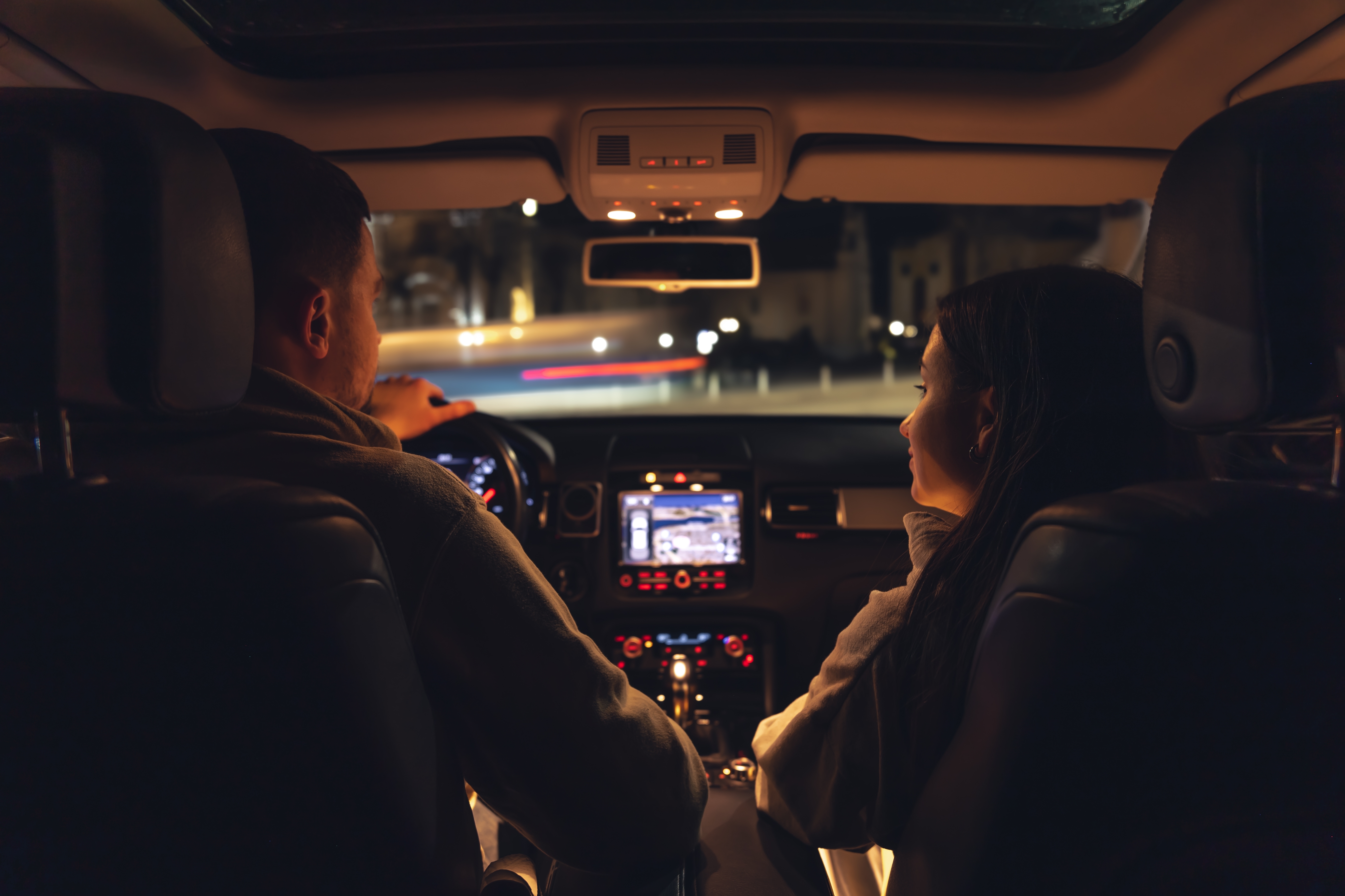 Un hombre y una mujer conducen de noche en un Automóvil, vista desde el coche hacia la carretera. | Fuente: Shutterstock