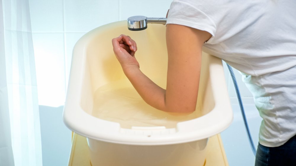 Mujer comprobando la temperatura del agua con su codo para bañar a su bebé. | Foto: Shutterstock
