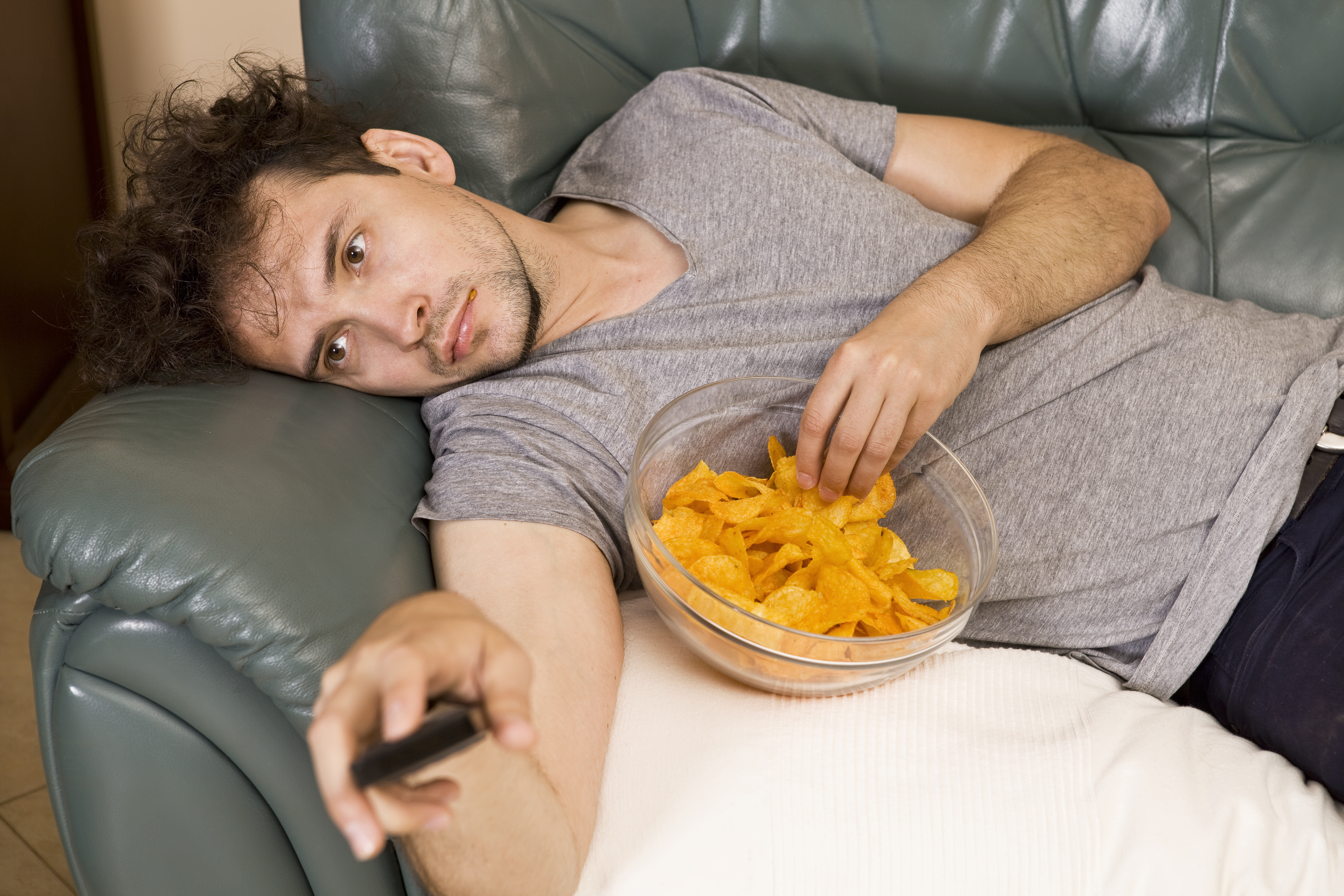 Un perezoso tumbado en un sofá viendo la televisión mientras come bocadillos | Fuente: Getty Images