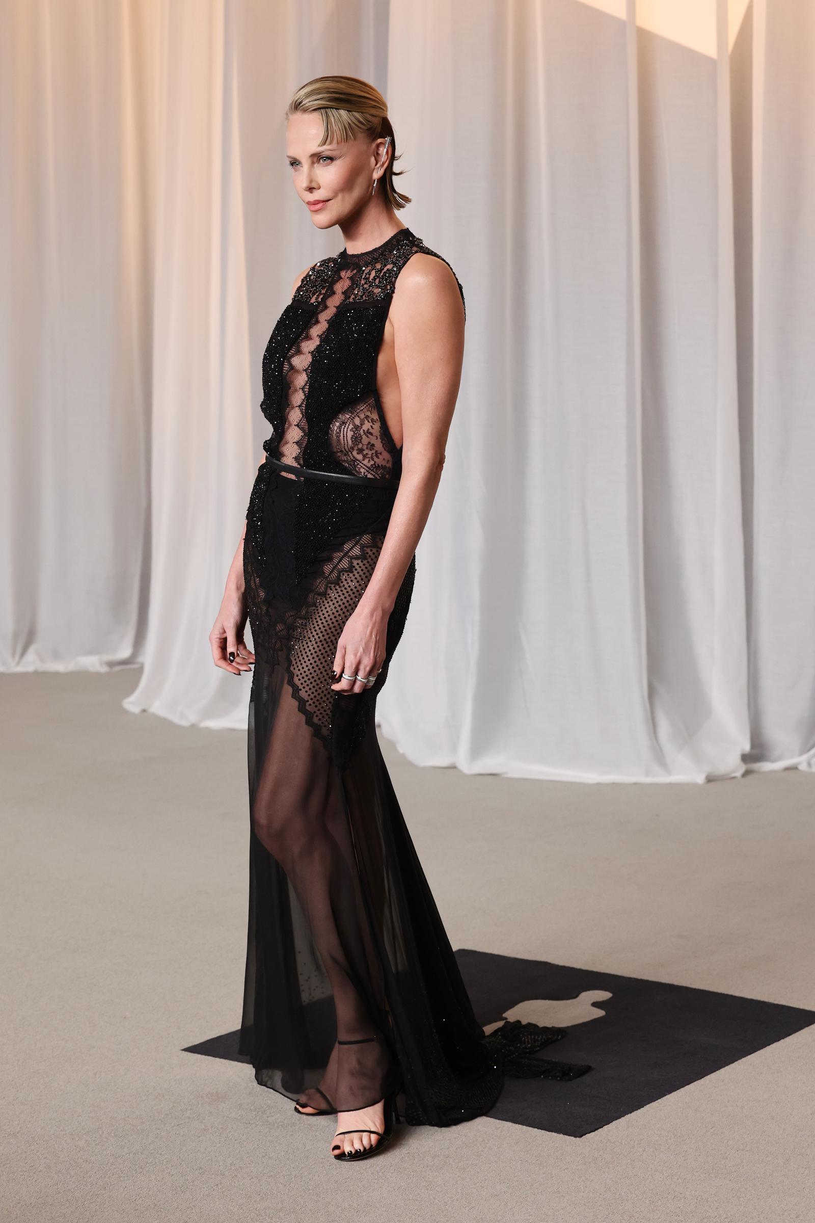 Charlize Theron aporta un toque dramático y atrevido a la alfombra roja con un vestido negro transparente sin mangas, con un intrincado diseño de capas de encaje delicado, abalorios y paneles de rejilla. Con un cinturón fino que le marca la cintura, un elegante recogido con efecto mojado y unas sandalias negras minimalistas, la ganadora del Óscar combina un glamour moderno y atrevido con el porte clásico de una estrella de cine mientras celebra haber recibido el Premio Icono.