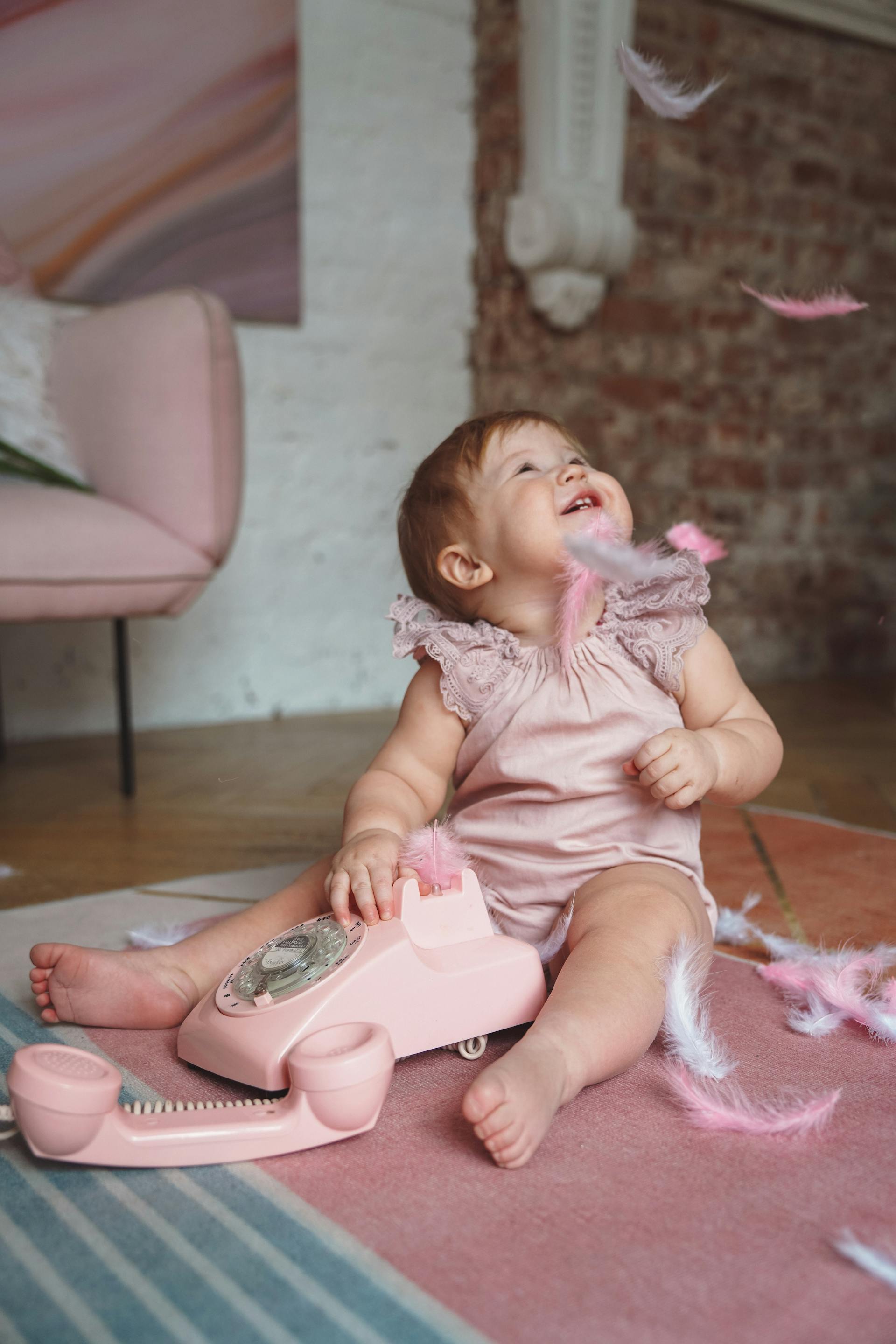 Una niña vestida de rosa jugando con plumas y un teléfono rosa