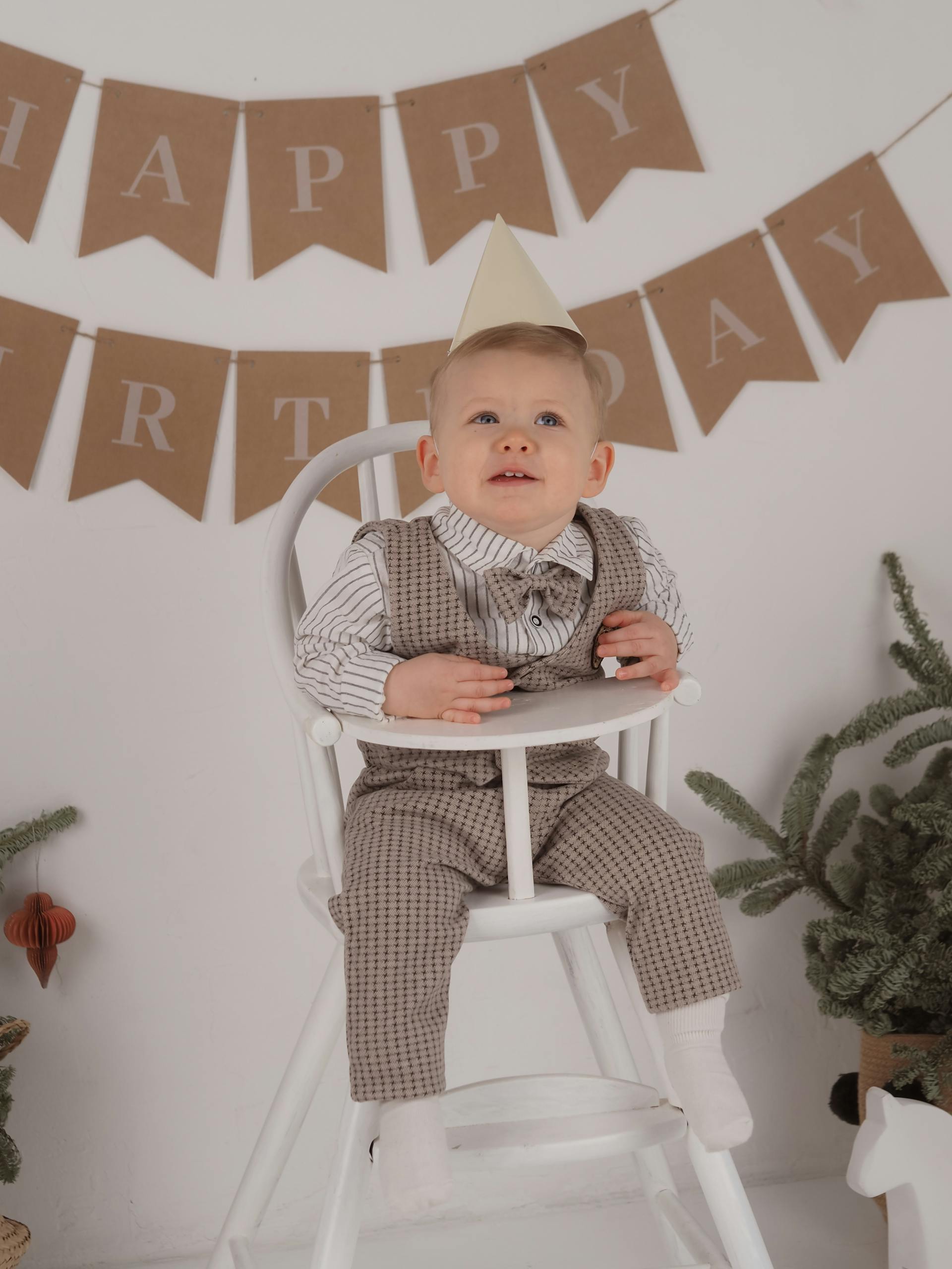 Un niño con un gorro de fiesta y sentado en una trona blanca el día de su cumpleaños | Fuente: Pexels