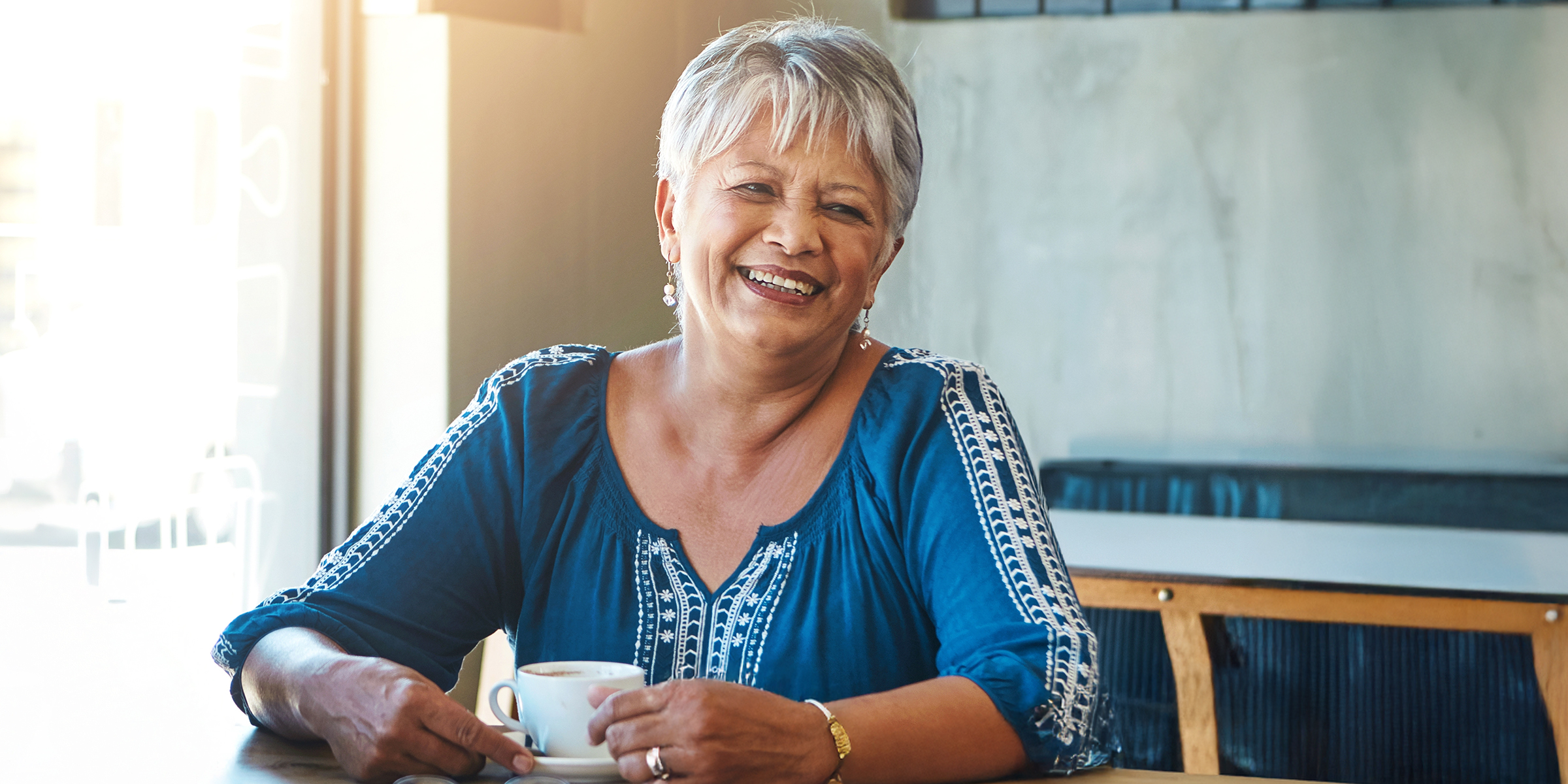 Una mujer mayor encantada con el pelo corto y canoso sentada en una mesa | Fuente: Shutterstock