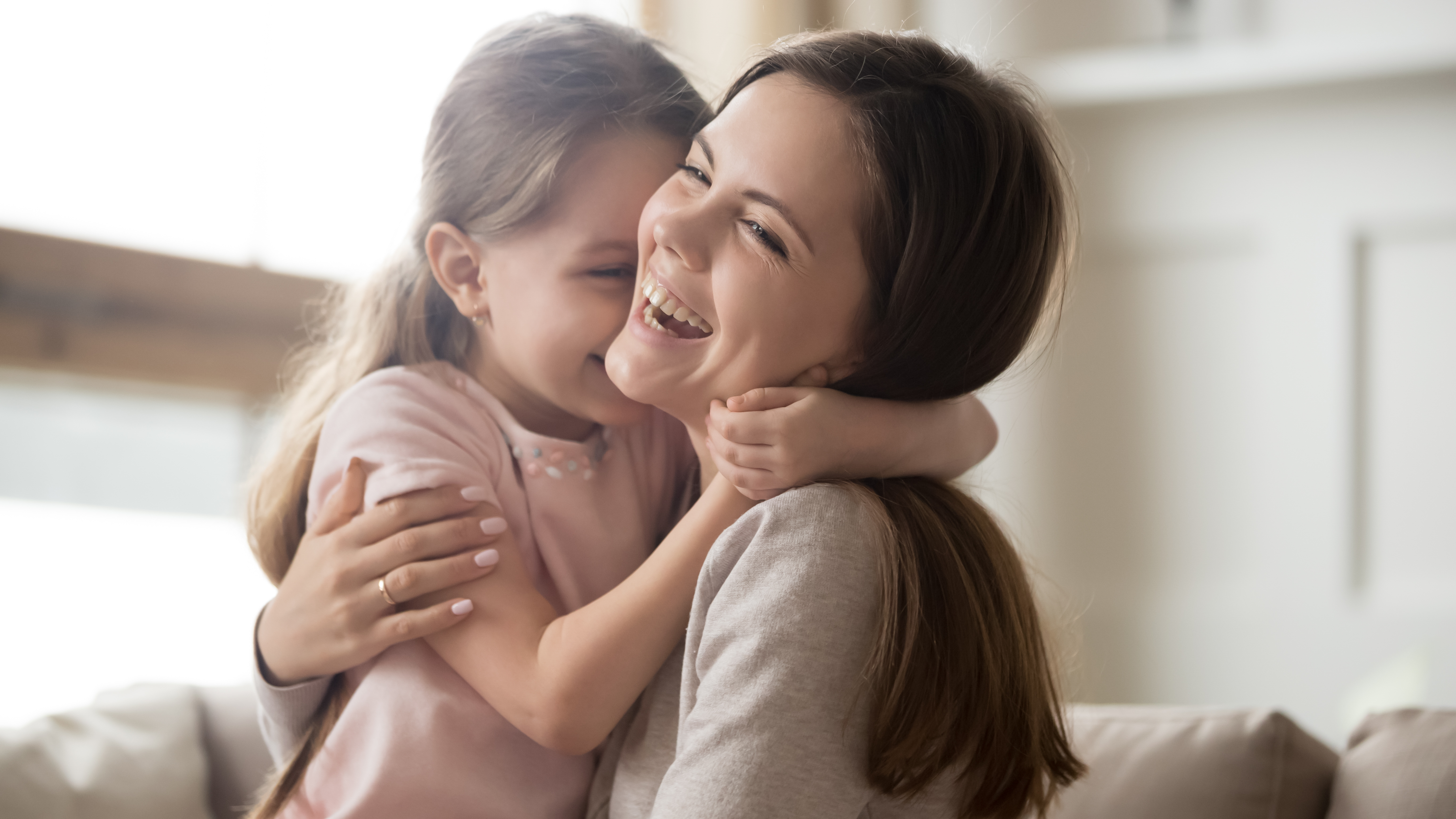 Joven madre cariñosa riendo abrazando sonriente a una niña graciosa | Foto: Getty Images