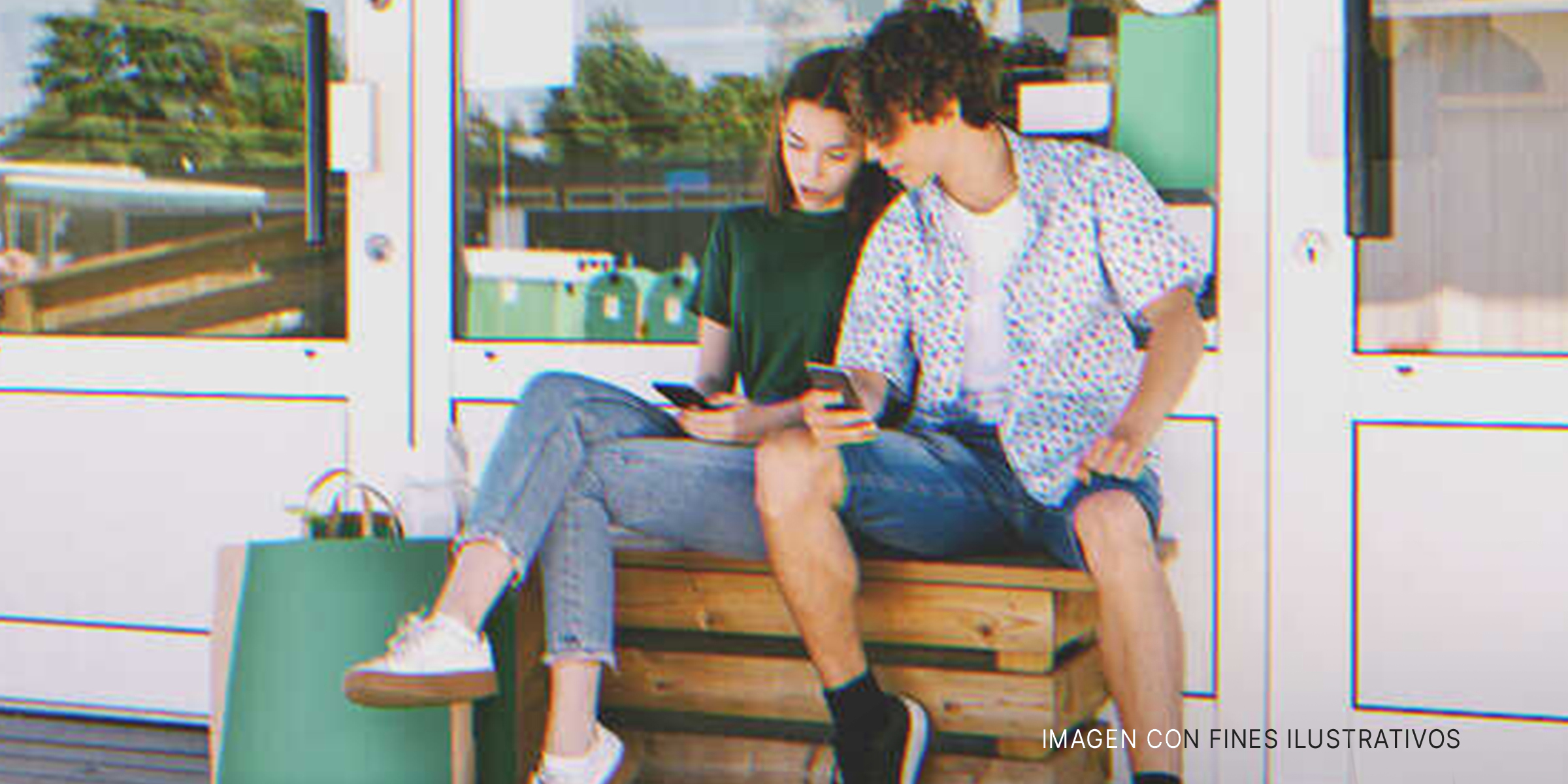 Un chico y una chica sentados al aire libre y mirando la pantalla de un teléfono. | Foto: Shutterstock