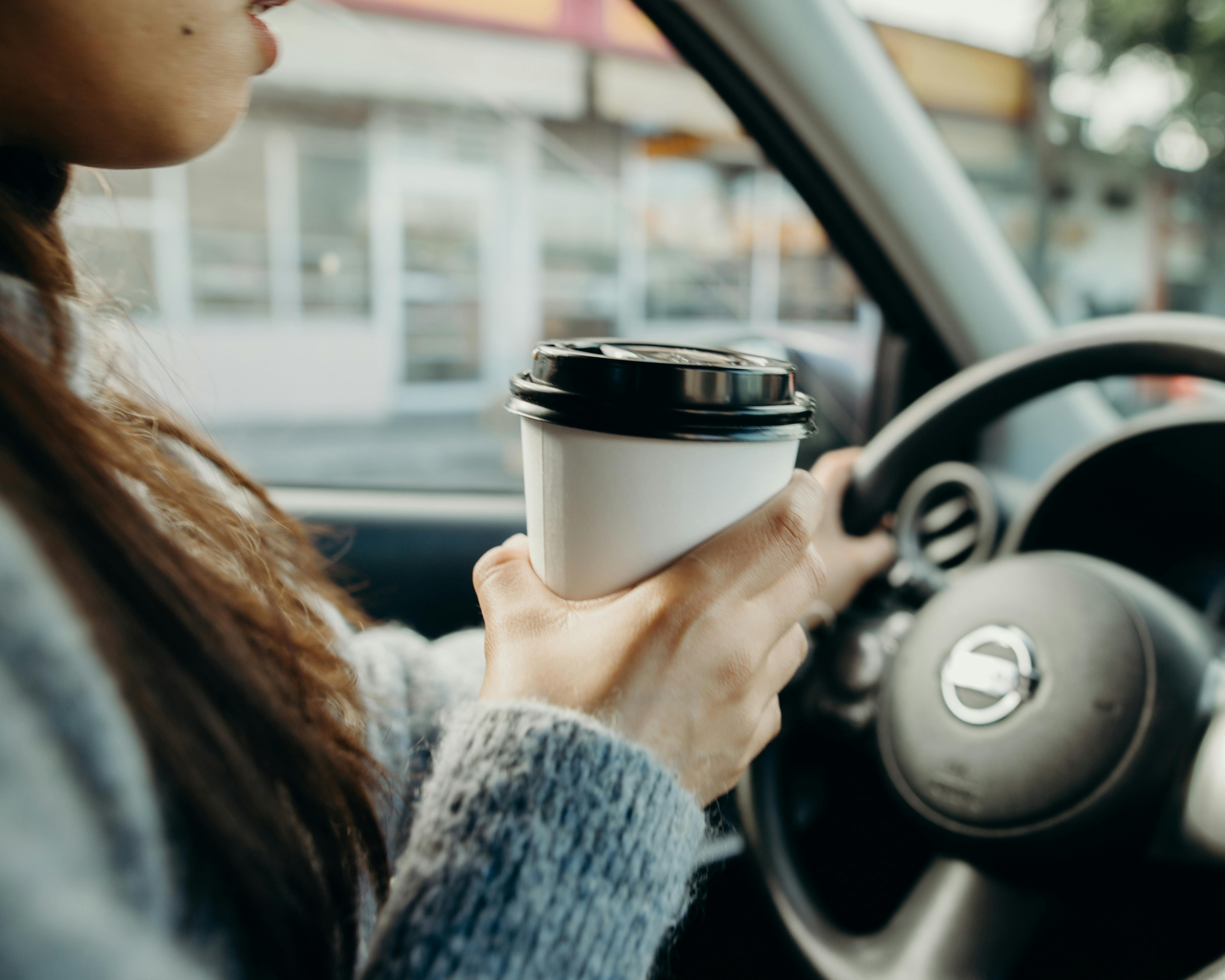 Una mujer conduciendo mientras sostiene un café | Fuente: Pexels