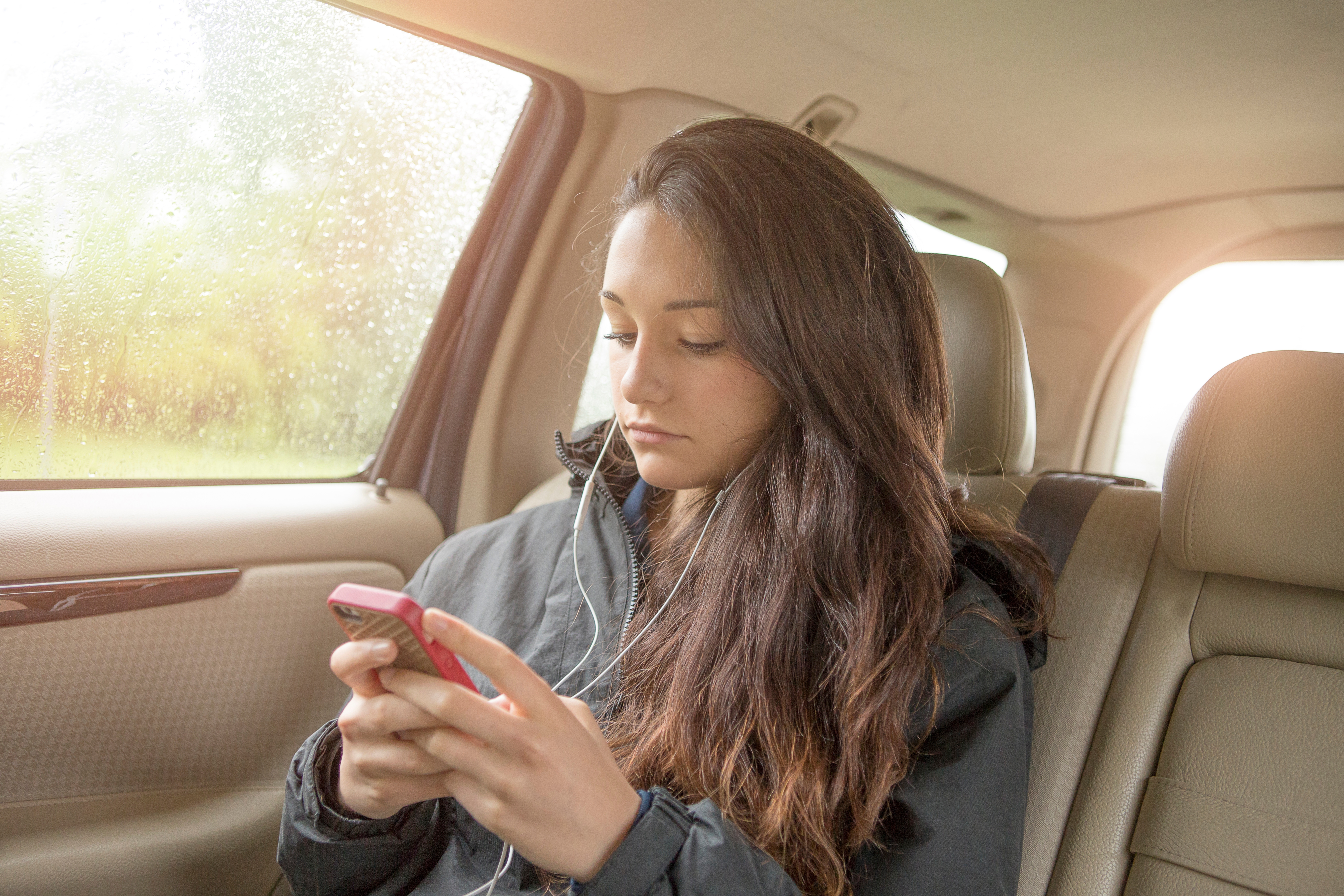 Adolescente con su smartphone en el asiento trasero del automóvil | Foto: Getty Images