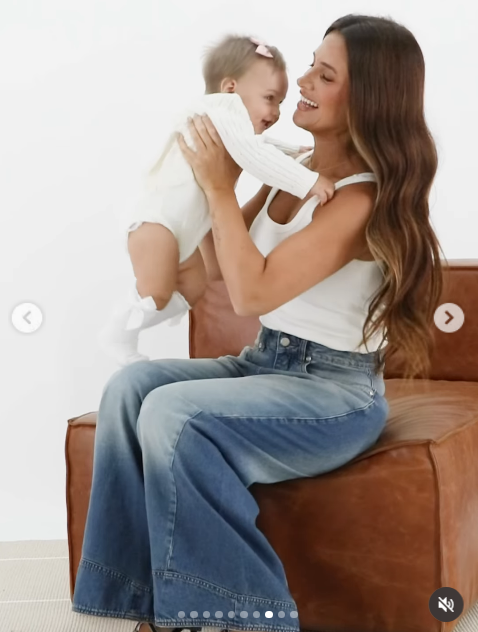 Sentada en un sillón individual color suela, Camila levantó dulcemente a Aitana a la altura de su rostro mientras compartían una mirada cómplice. El encuadre resalta el estilismo relajado de ambas en tonos blancos y denim para la cápsula de calzado y accesorios. | Fuente: Instagram/camihoms