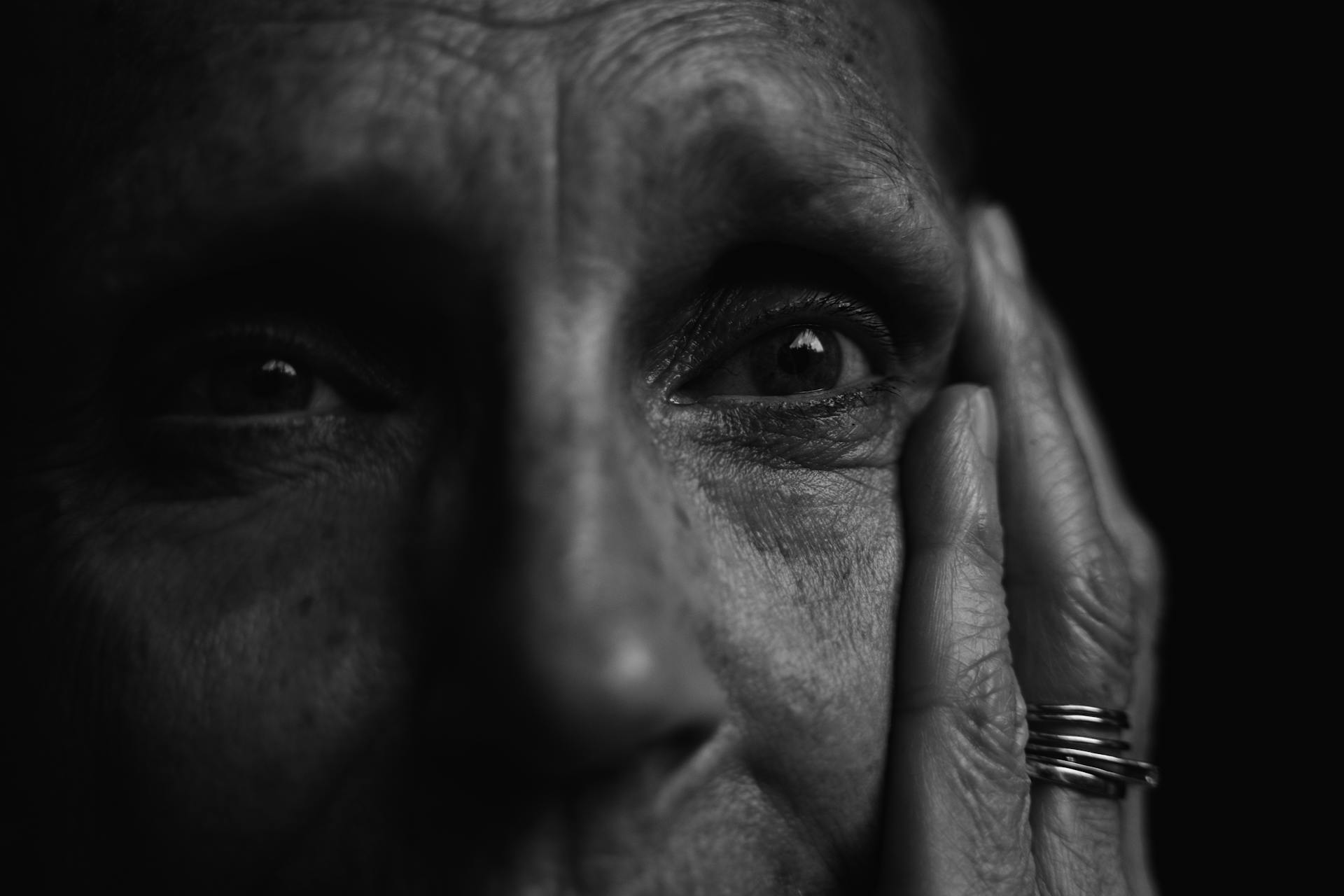 Scatto in scala di grigi di una persona anziana emozionata che si tiene il viso... Fonte: Pexels
