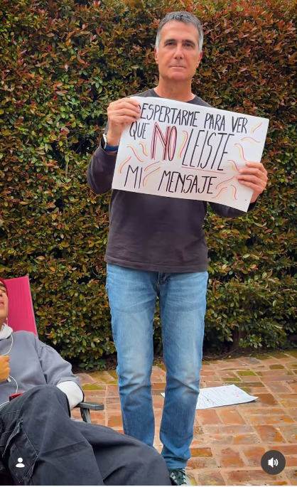 Mirando seriamente al frente, Antonio Laje sostuvo firmemente con ambas manos el cartel con la frase "DESPERTARME PARA VER QUE NO LEÍSTE MI MENSAJE". En la escena del video musical casero se observan las hojas ya descartadas sobre el suelo de ladrillos y a su hijo descansando en el lateral. | Fuente: Instagram/leish.ar