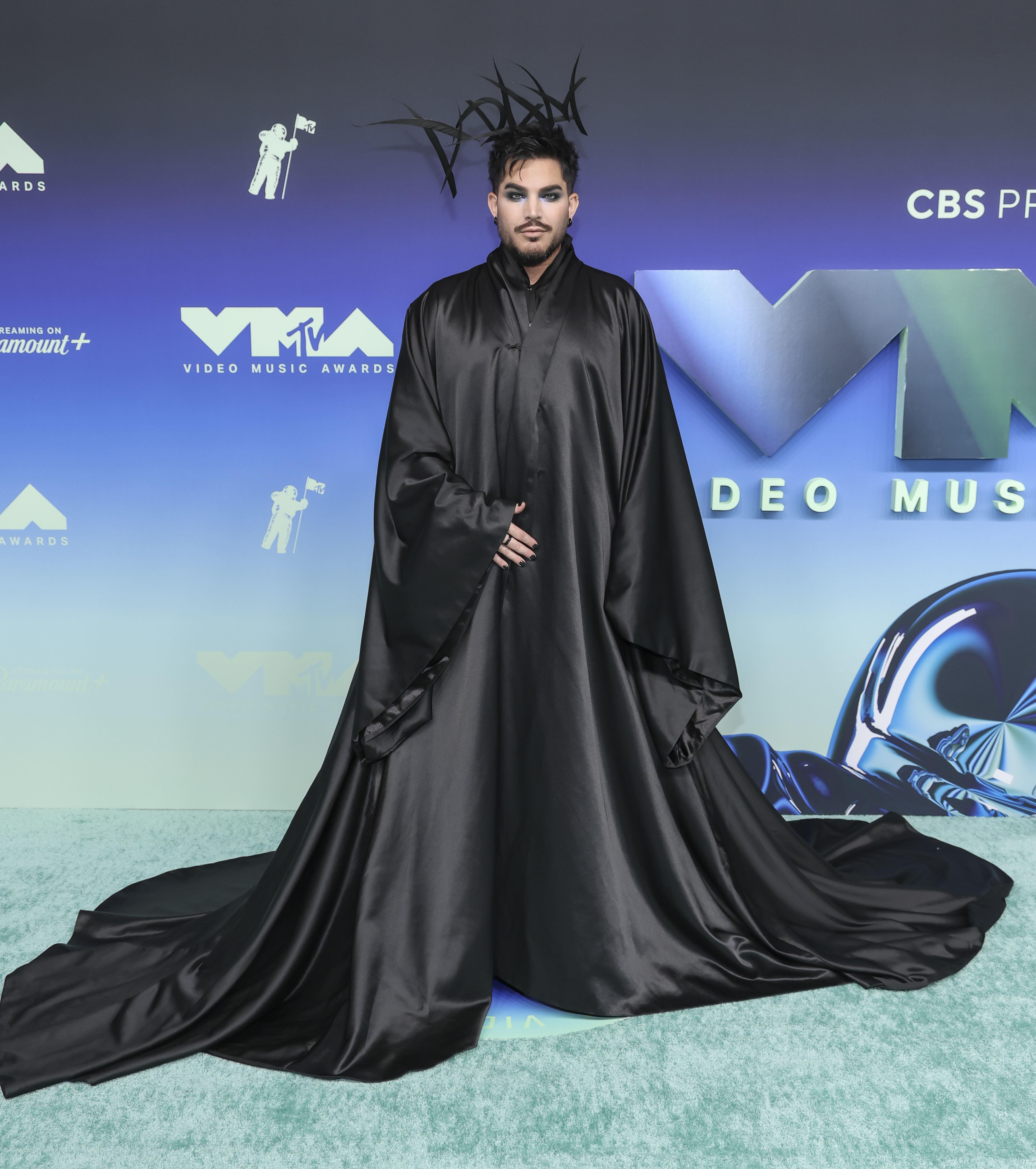 Lambert posó bajo una espectacular tela negra que caía en una amplia onda, mientras su capa, que le llegaba hasta el suelo, se extendía sobre la alfombra. Los largos mechones puntiagudos de su pelo alargaban la silueta hacia arriba, creando un marcado contraste con la forma amplia de la capa por debajo. | Fuente: Getty Images
