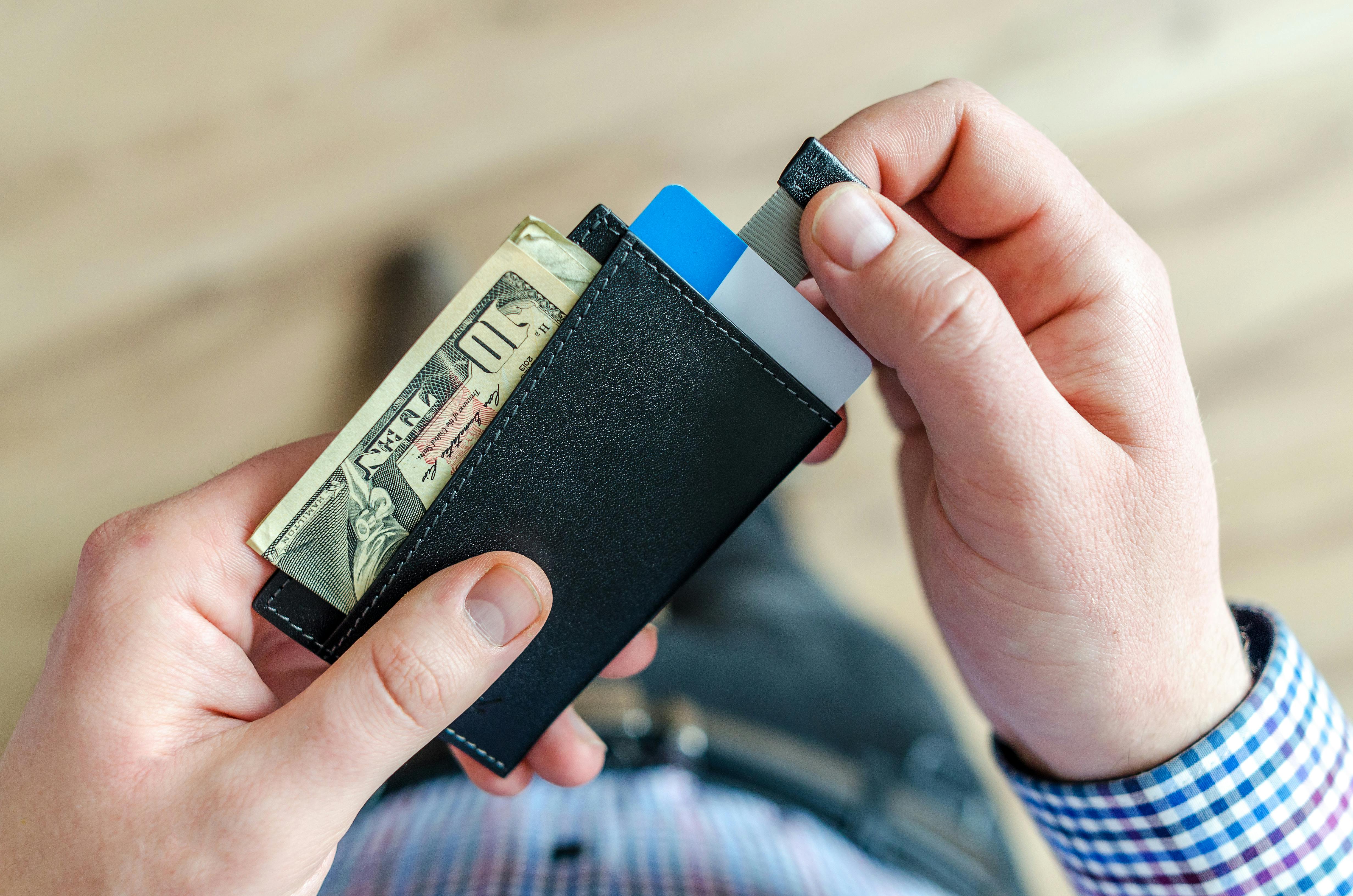 Un hombre sostiene una cartera con tarjetas bancarias y dinero | Fuente: Pexels
