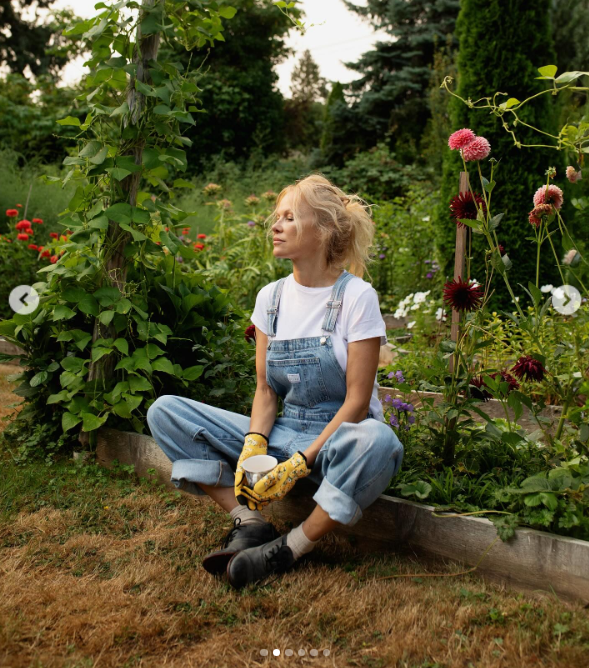 Pamela Anderson se toma un momento para reflexionar tranquilamente en su jardín, sentada con las piernas cruzadas en un parterre elevado, vestida con un mono vaquero, guantes de flores y botas con cordones, mientras sostiene una taza bajo el sol de la tarde. Rodeada de altas dalias en flor, una exuberante vegetación y judías trepadoras, compartió esta tranquila imagen junto con una nota en la que describía su serie de cocina "Pamela's Cooking with Love" como "diversión, diversión, diversión". | Fuente: Instagram/pamelaanderson