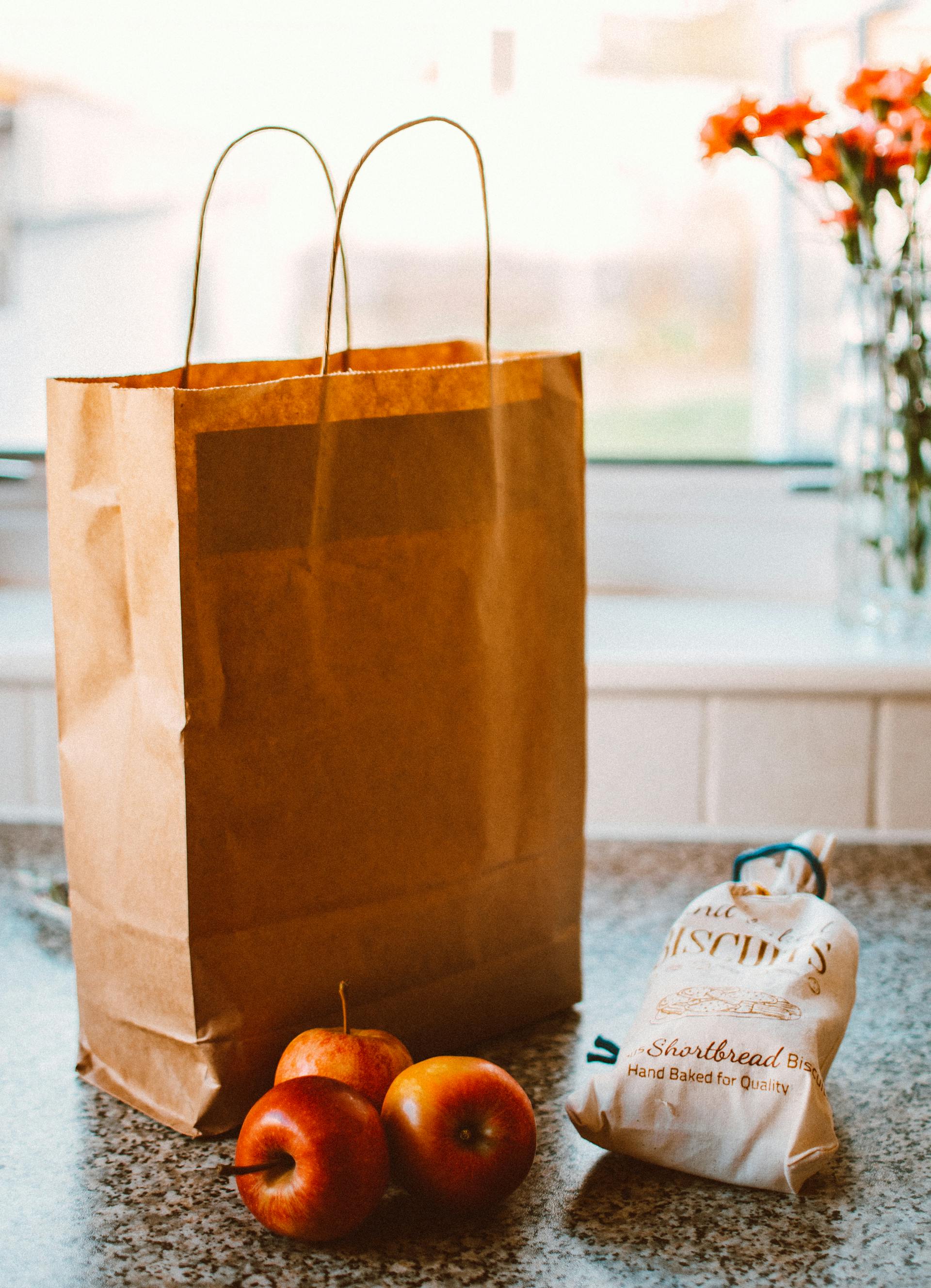 Varias manzanas junto a una bolsa de papel marrón y un paquete de pan | Fuente: Pexels
