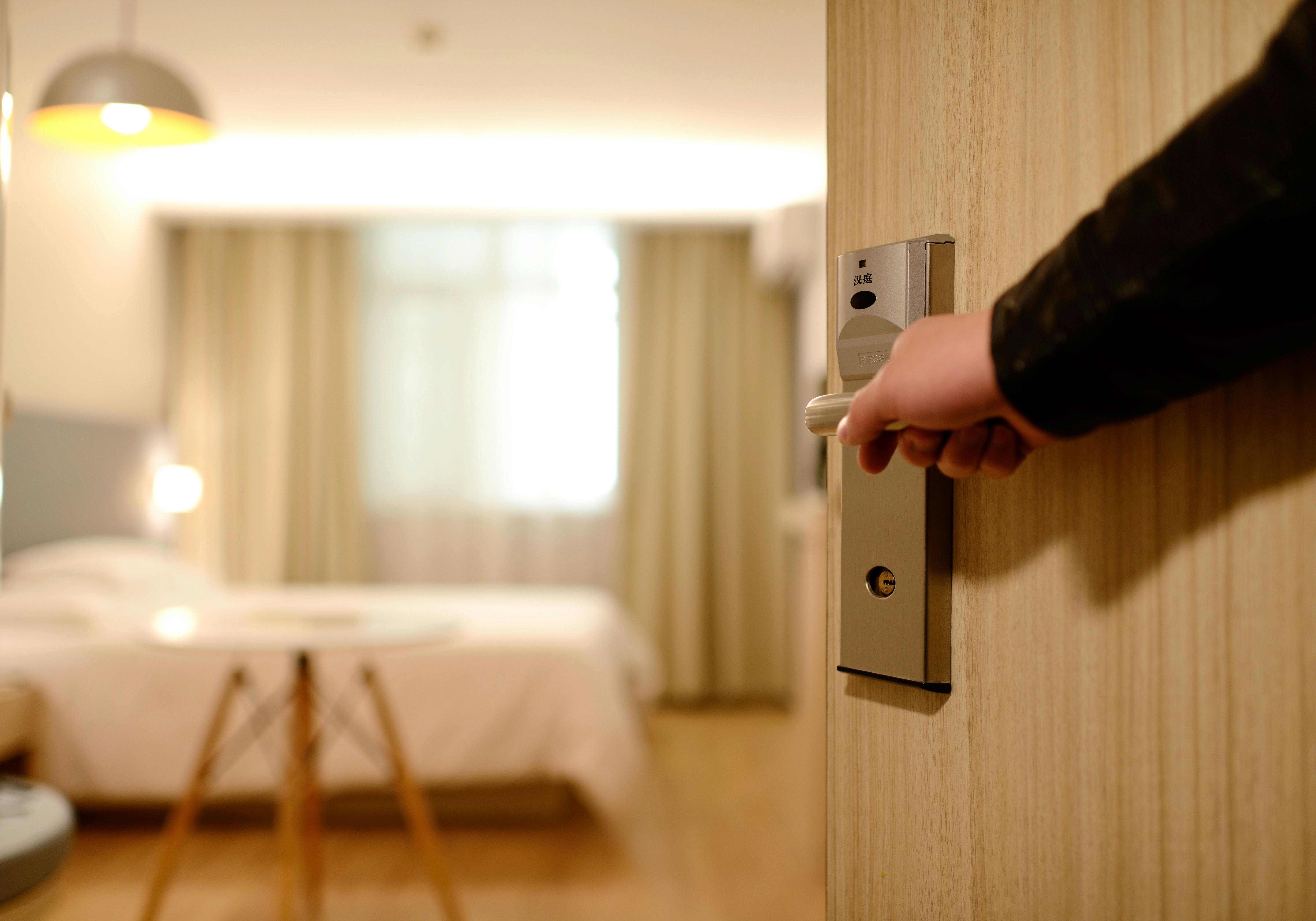 Una persona mantiene abierta la puerta de una habitación de hotel | Fuente: Pexels