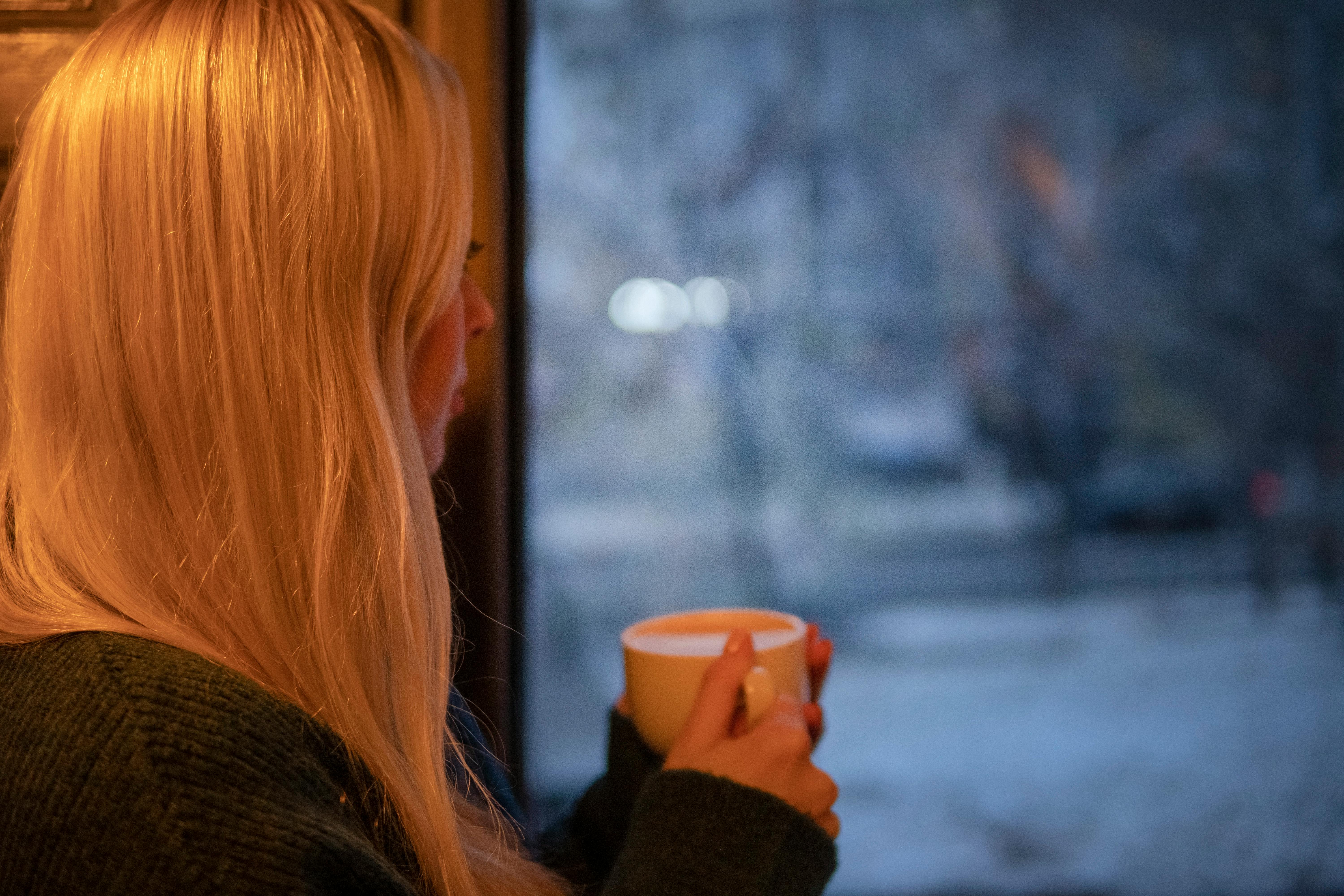 Una chica con una taza de café mirando por la ventana | Fuente: Pexels