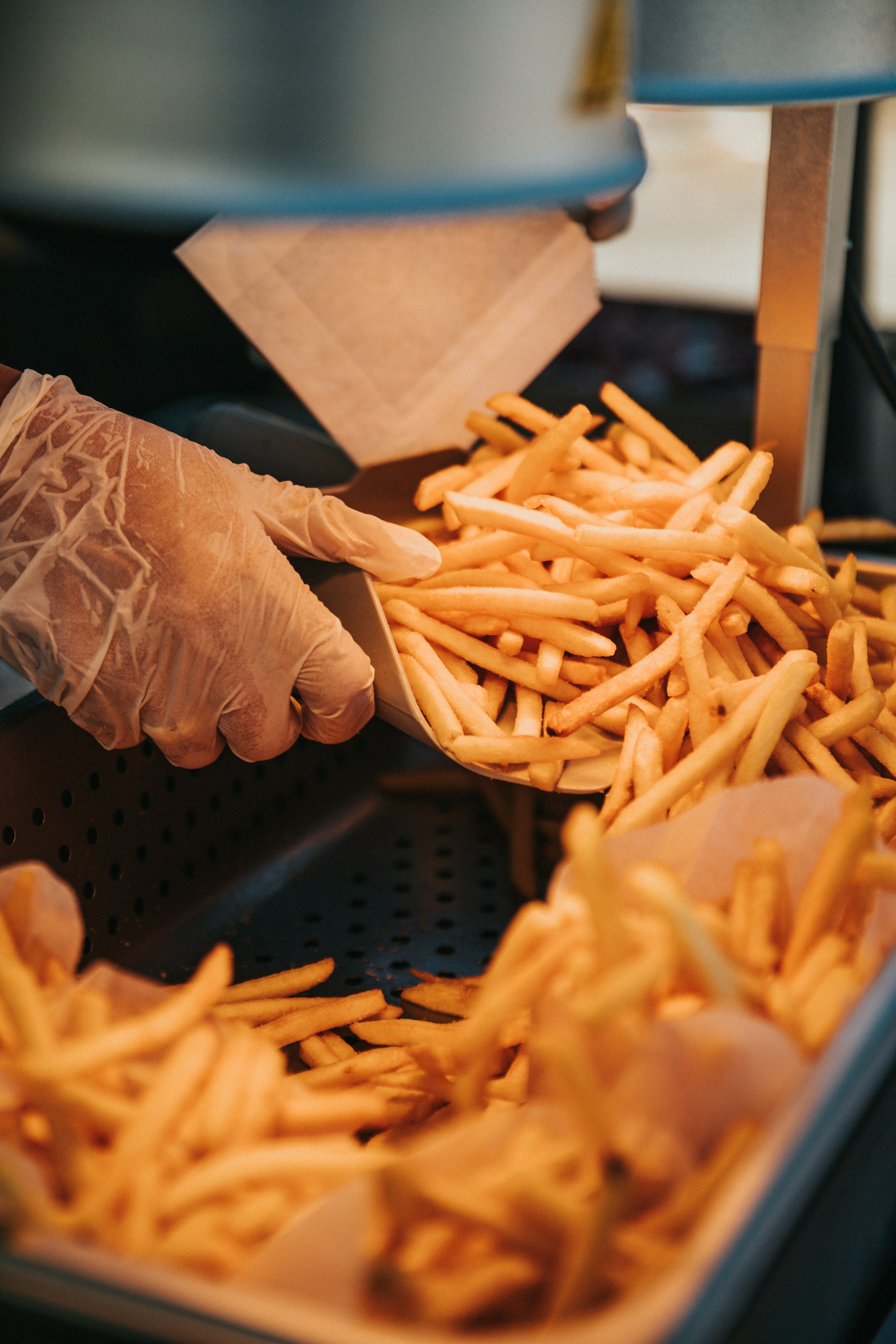 Una persona con una mano enguantada sacando patatas fritas de una bandeja | Fuente: Unsplash