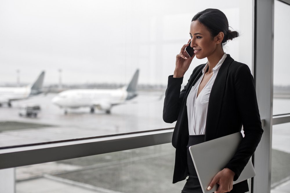  Mujer hablando por teléfono usando un blazer negro y falta negra sosteniendo una portátil. | Foto: Shutterstock